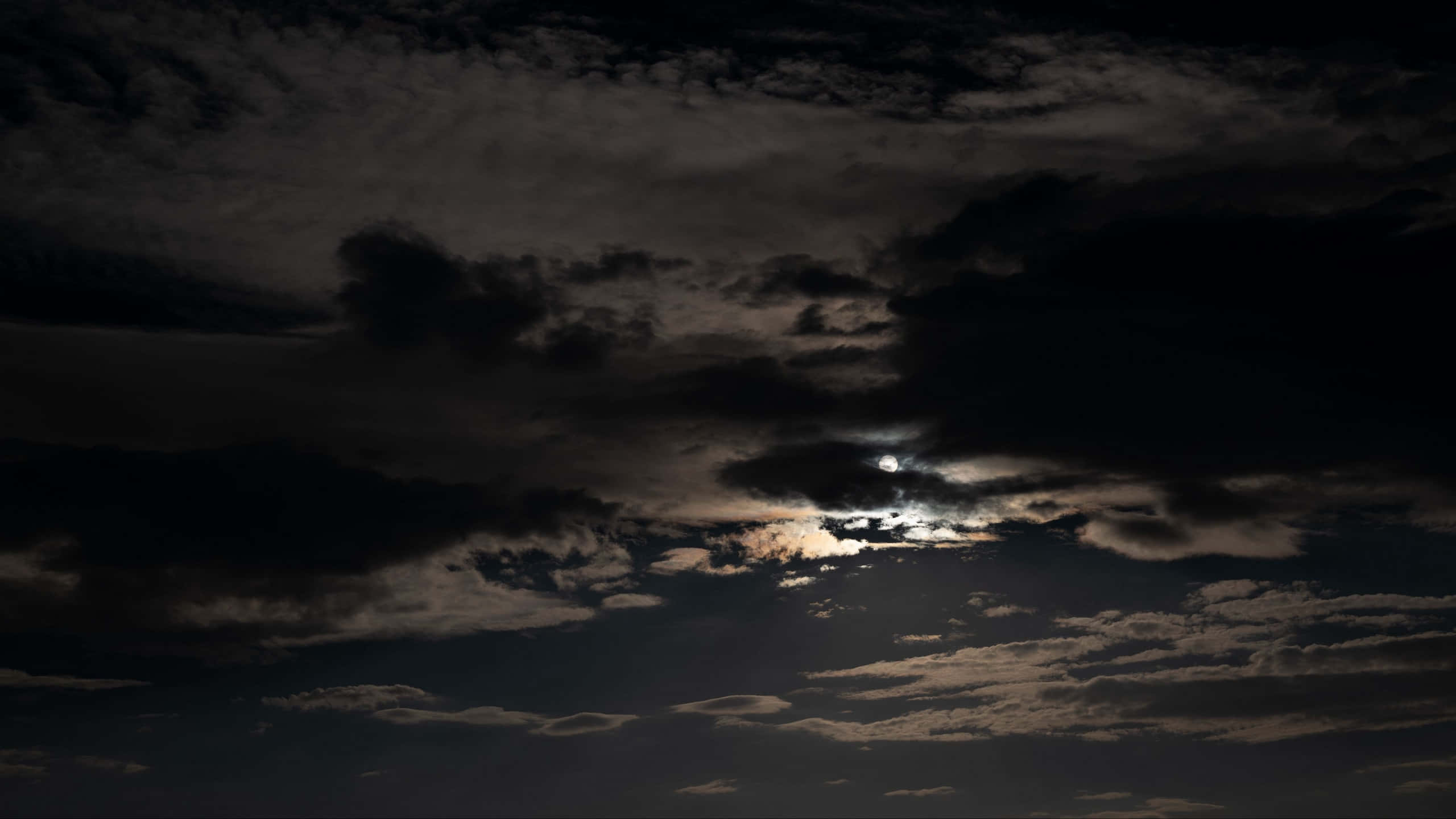 Dark Night 桌布 壁紙 — 一輪明亮的月亮穿透濃密的烏雲，在陰鬱的夜空中灑下空靈的光芒。