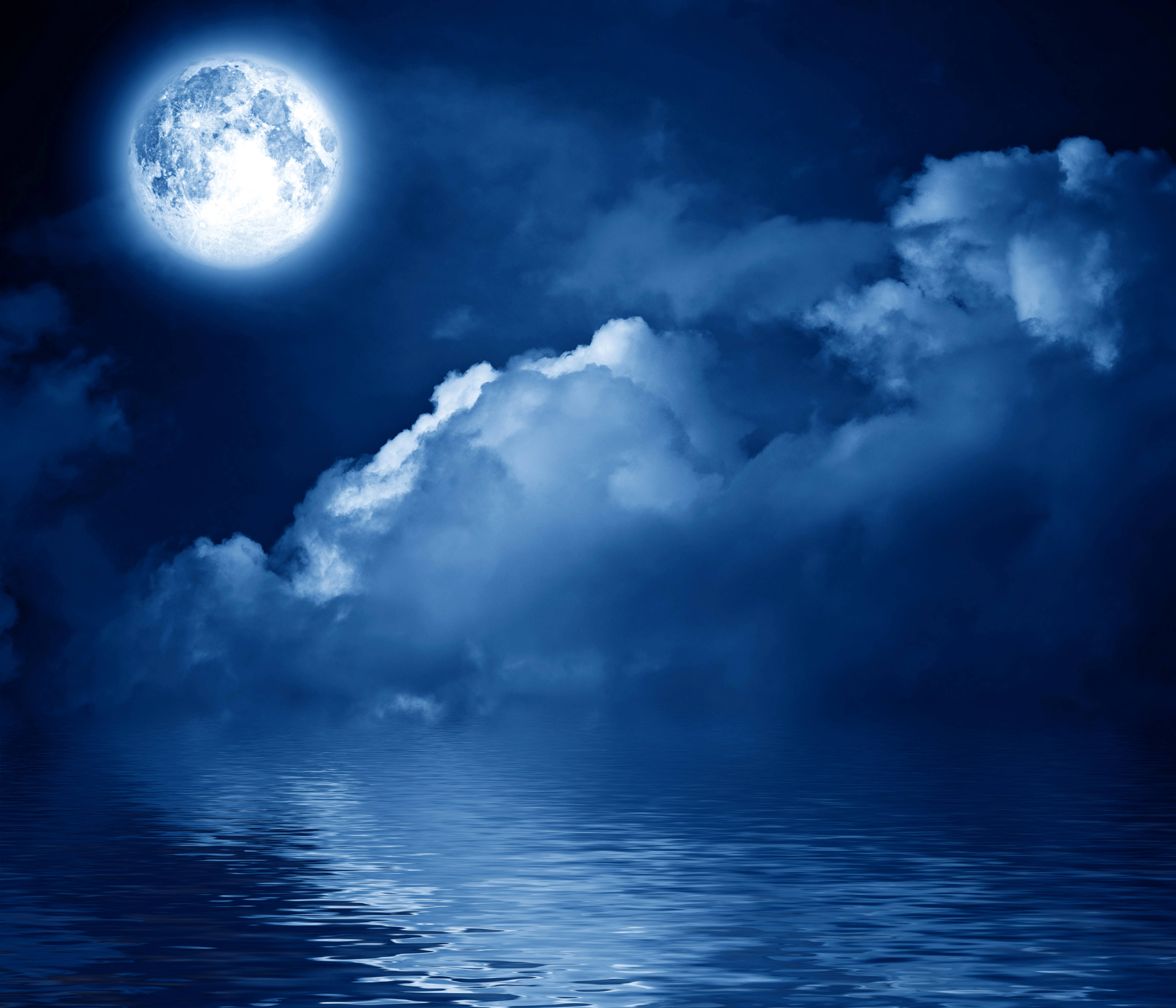 夜空 桌布 壁紙 — 一輪明亮的滿月在平靜的海洋上投下寧靜的藍色光芒，蓬鬆的雲朵在夜空中飄移。