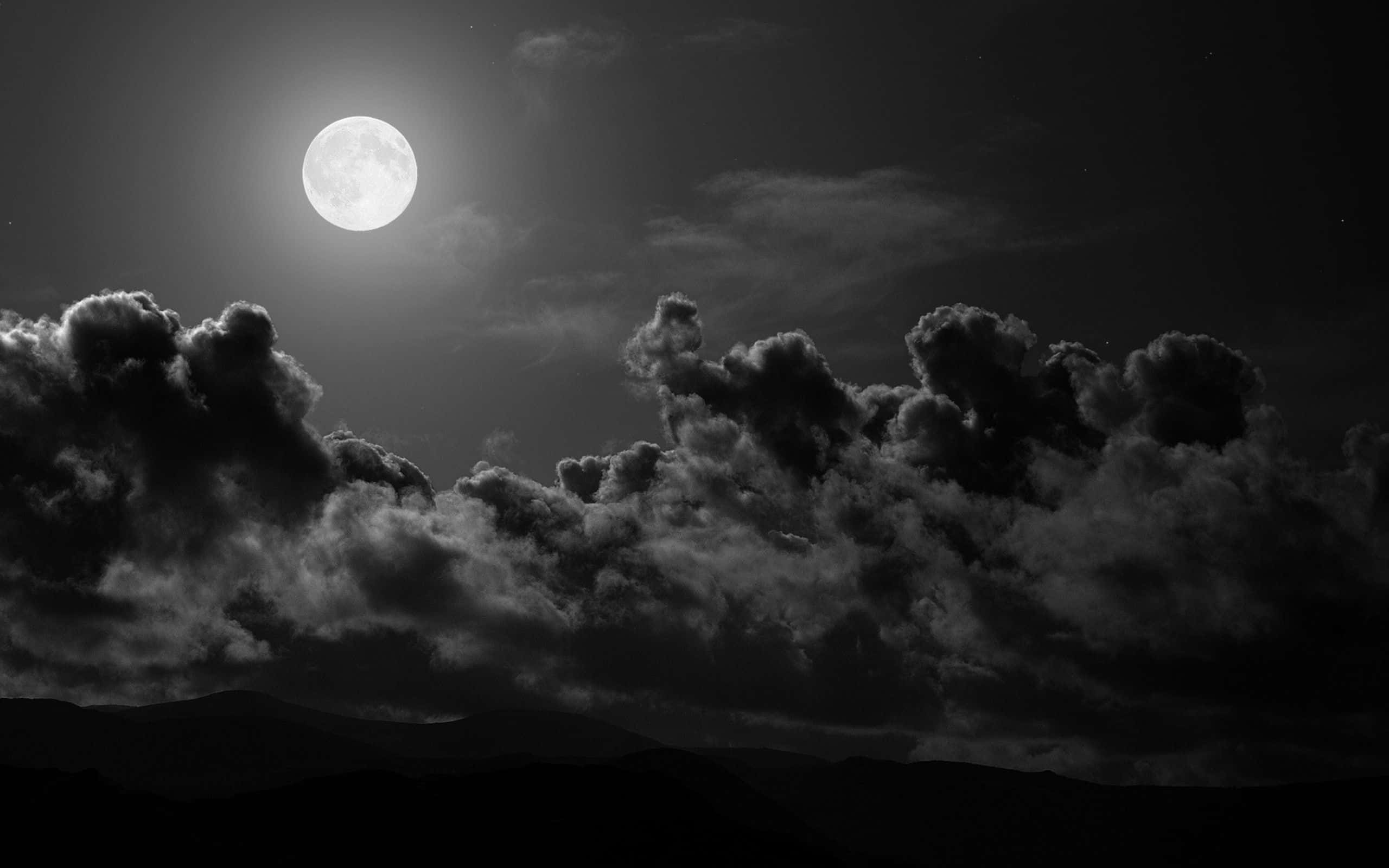 Dark Moon 桌布 壁紙 — 一輪明亮的滿月在戲劇性、紋理豐富的雲層上投下鮮明的光芒，雲層在黑暗的山脈背景下形成剪影。