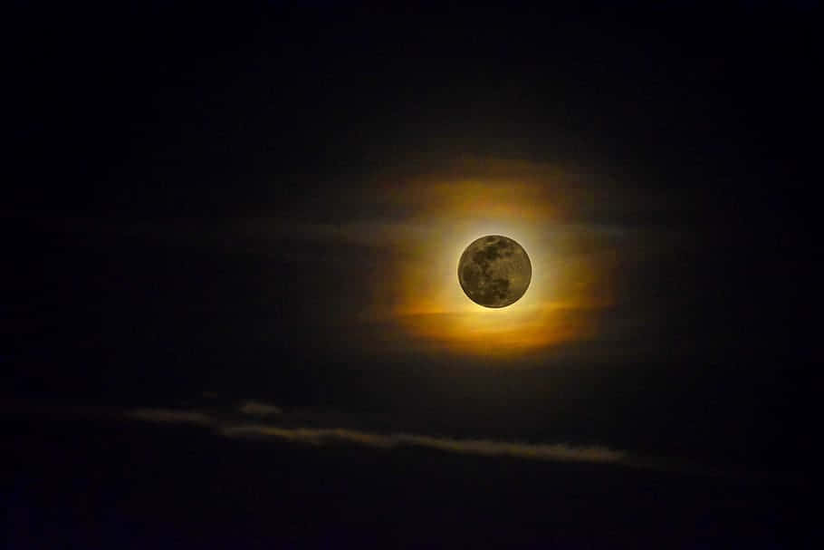 Perigee 桌布 壁紙 — 一輪明亮的滿月散發著金色光暈，映襯著佈滿薄雲的漆黑夜空。