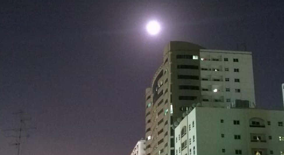 Perigee 桌布 壁紙 — 一輪明亮的滿月照耀著夜晚中一簇現代公寓樓，部分窗戶亮著燈。