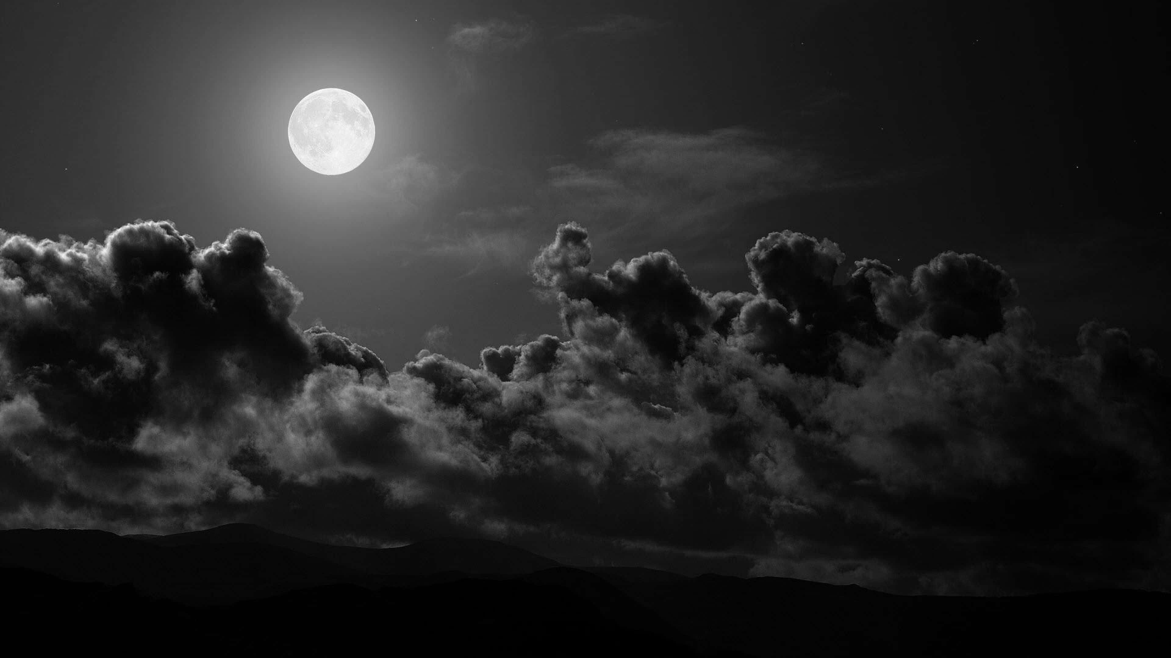 Dark Sky 桌布 壁紙 — 一輪明亮的滿月穿過戲劇性的雲層，照耀在剪影般的山脈之上，構成鮮明的黑白夜景。