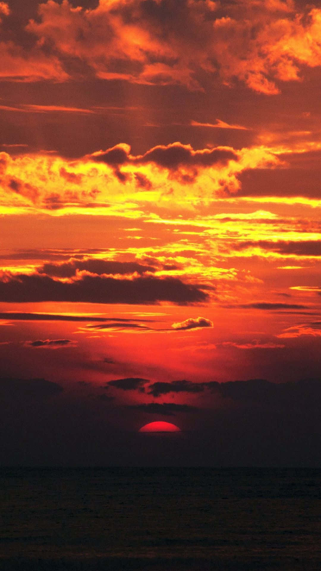 Red Sunset 桌布 壁紙 — 一輪火紅的夕陽將天空染成鮮豔的橙色和紅色，太陽在平靜的海洋上沉入地平線以下。