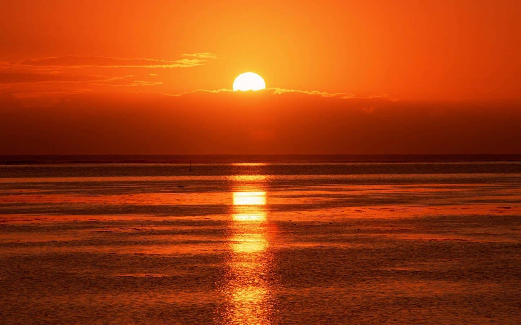 海灘日落 桌布 壁紙 — 一輪火紅的橙色太陽在平靜的海洋上落下，在水面上投射出燦爛的倒影。