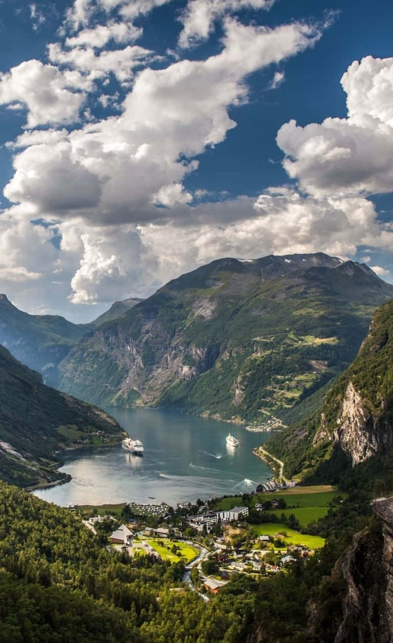Norway 桌布 壁紙 — 一道令人屏息的峽灣蜿蜒穿過高聳的綠色山脈，上方是明亮的藍天和蓬鬆的白雲。