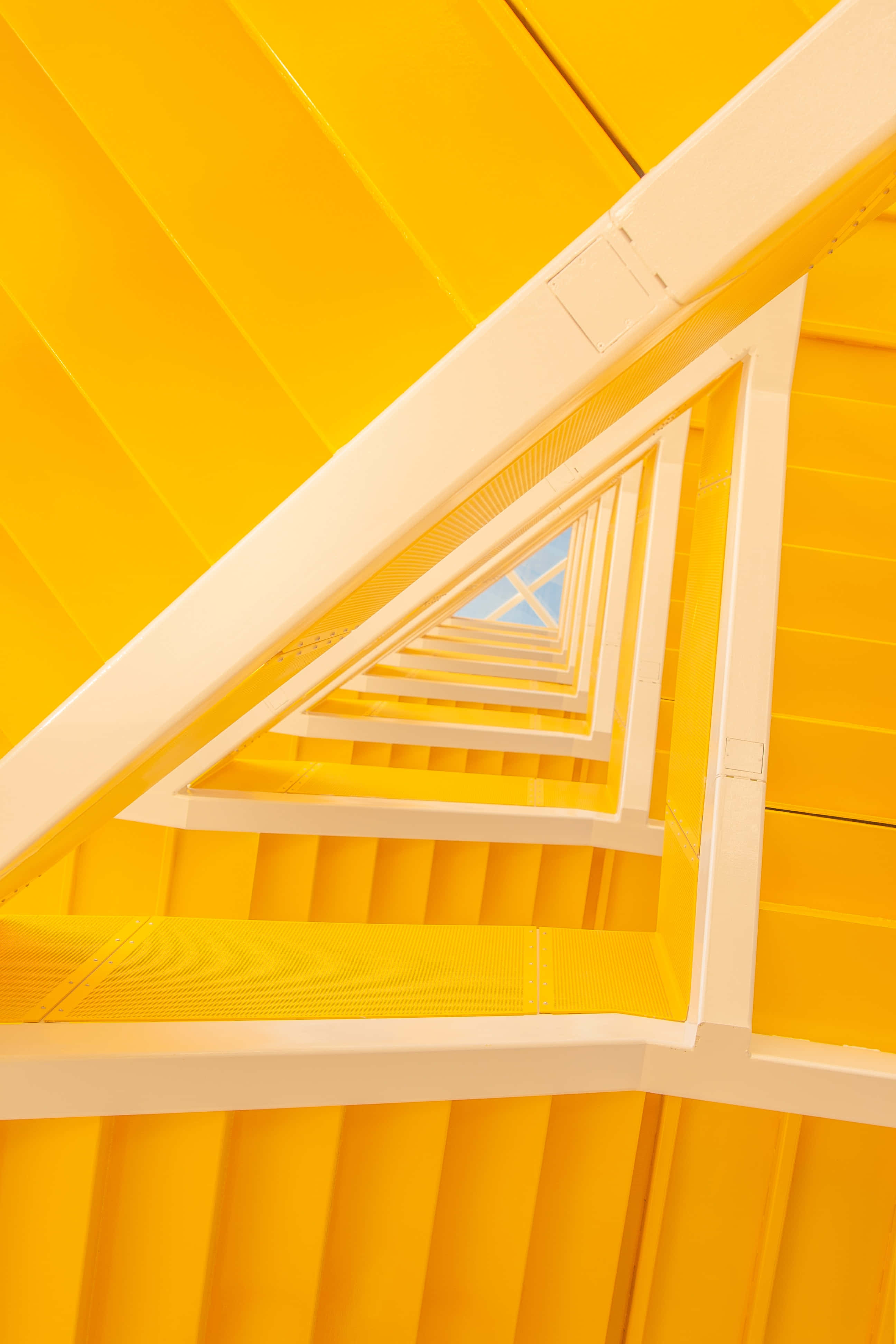 Yellow Triangle 桌布 壁紙 — 一道充滿活力的黃色樓梯以幾何圖案螺旋向上，由潔白的欄杆框著，通往一小片藍天。