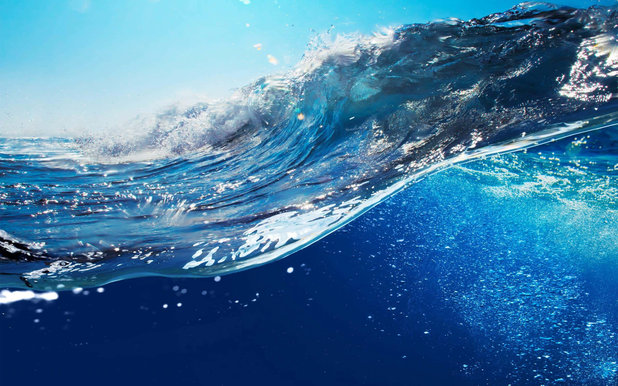 waves 桌布 壁紙 — 一道動態的海浪在頭頂翻捲，陽光照射的水花在清澈的藍天和深邃的水下景色中飛濺。