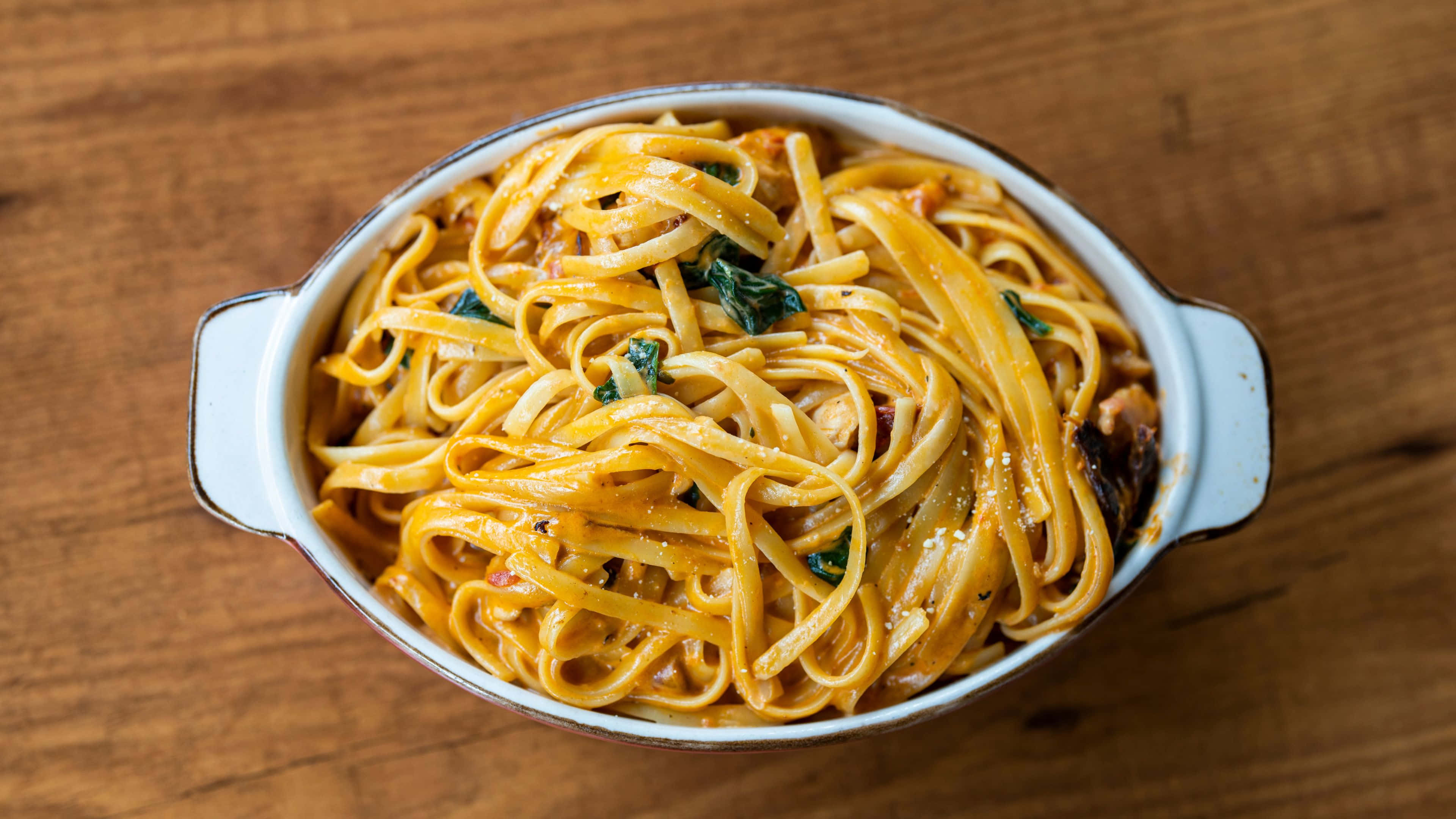 Noodles 桌布 壁紙 — 一道奶油菠菜番茄醬意粉，盛載於白色陶瓷碗中，放在木桌上。