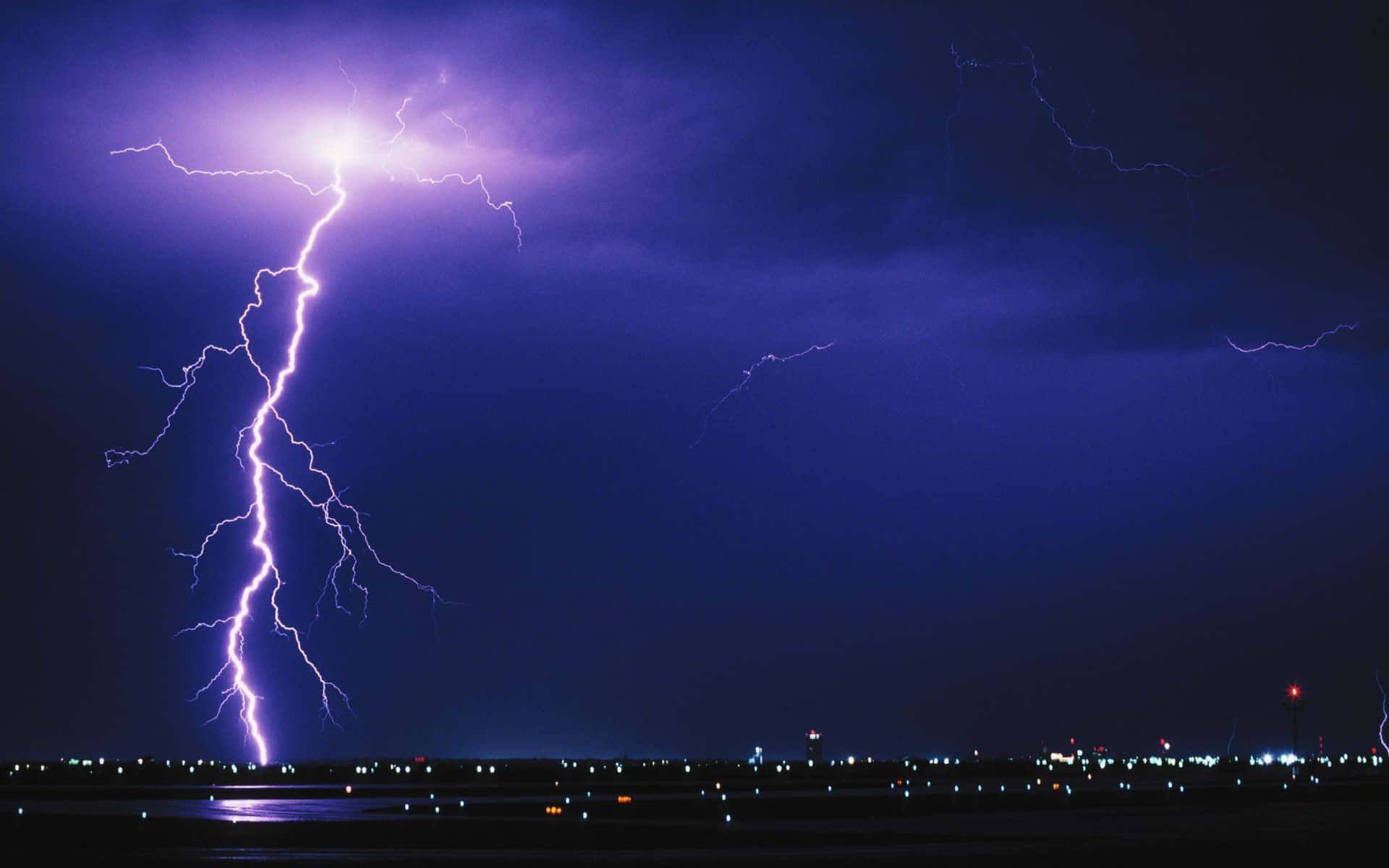 Thunderstorm 桌布 壁紙 — 一道巨大的紫色閃電在夜間劃過黑暗的城市景觀，照亮了下方的雲層和遠處的燈光。