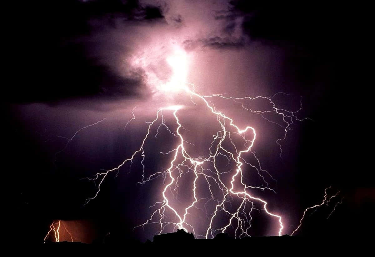 Thunderstorm 桌布 壁紙 — 一道巨大的閃電在黑暗的暴風雨天空中分叉，照亮了紫色的雲層和下方的山丘輪廓。