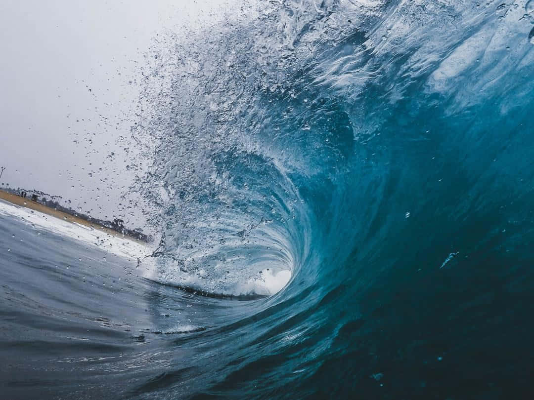 waves 桌布 壁紙 — 一道強勁的海浪在灰色的天空下捲成一個玻璃般的藍色管狀，帶有泡沫般的白色飛沫。