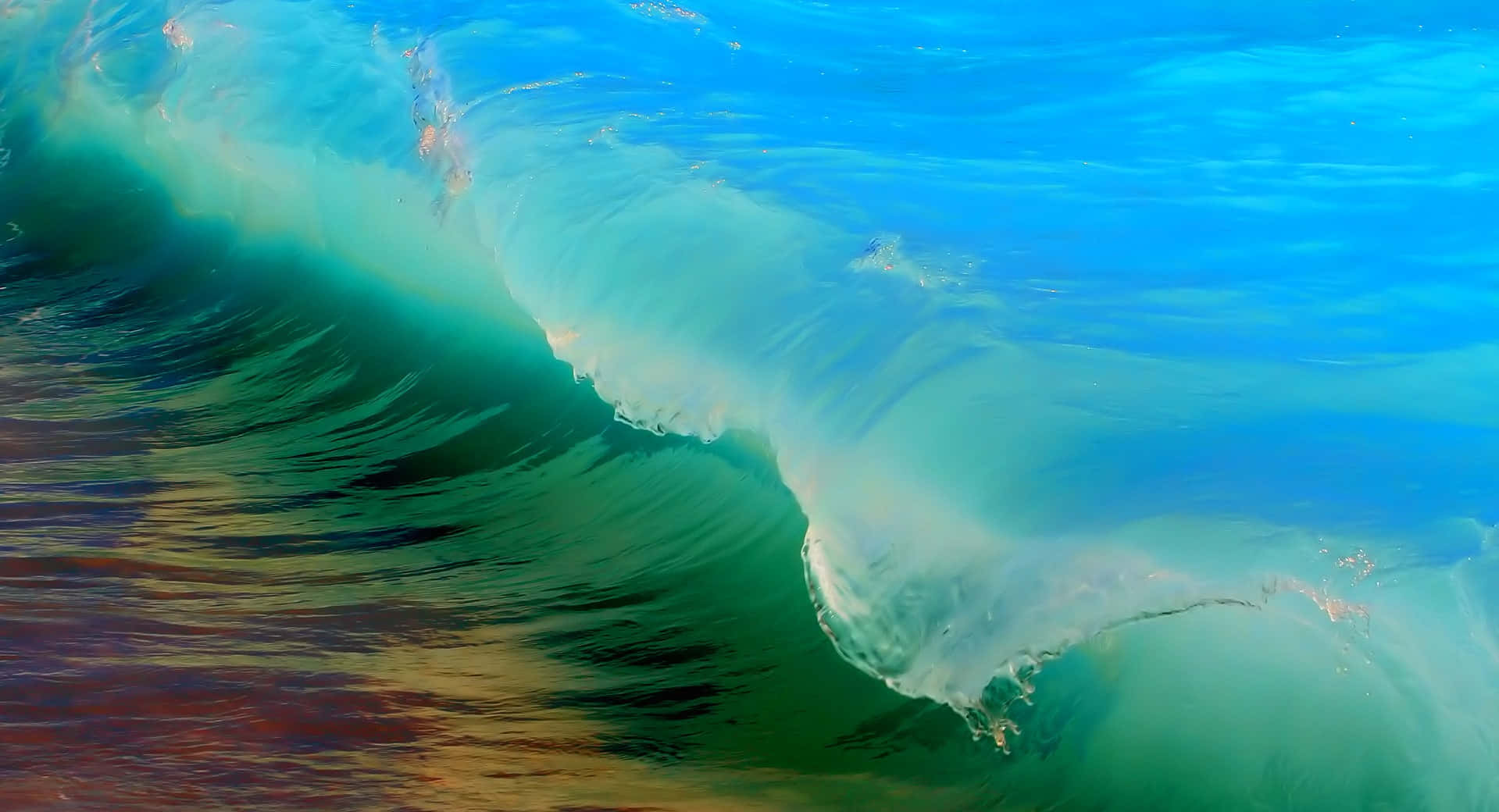 Beach Waves 桌布 壁紙 — 一道強勁的海浪捲成半透明的綠色筒狀，上方是鮮豔的藍色海水，下方是溫暖的大地色調。