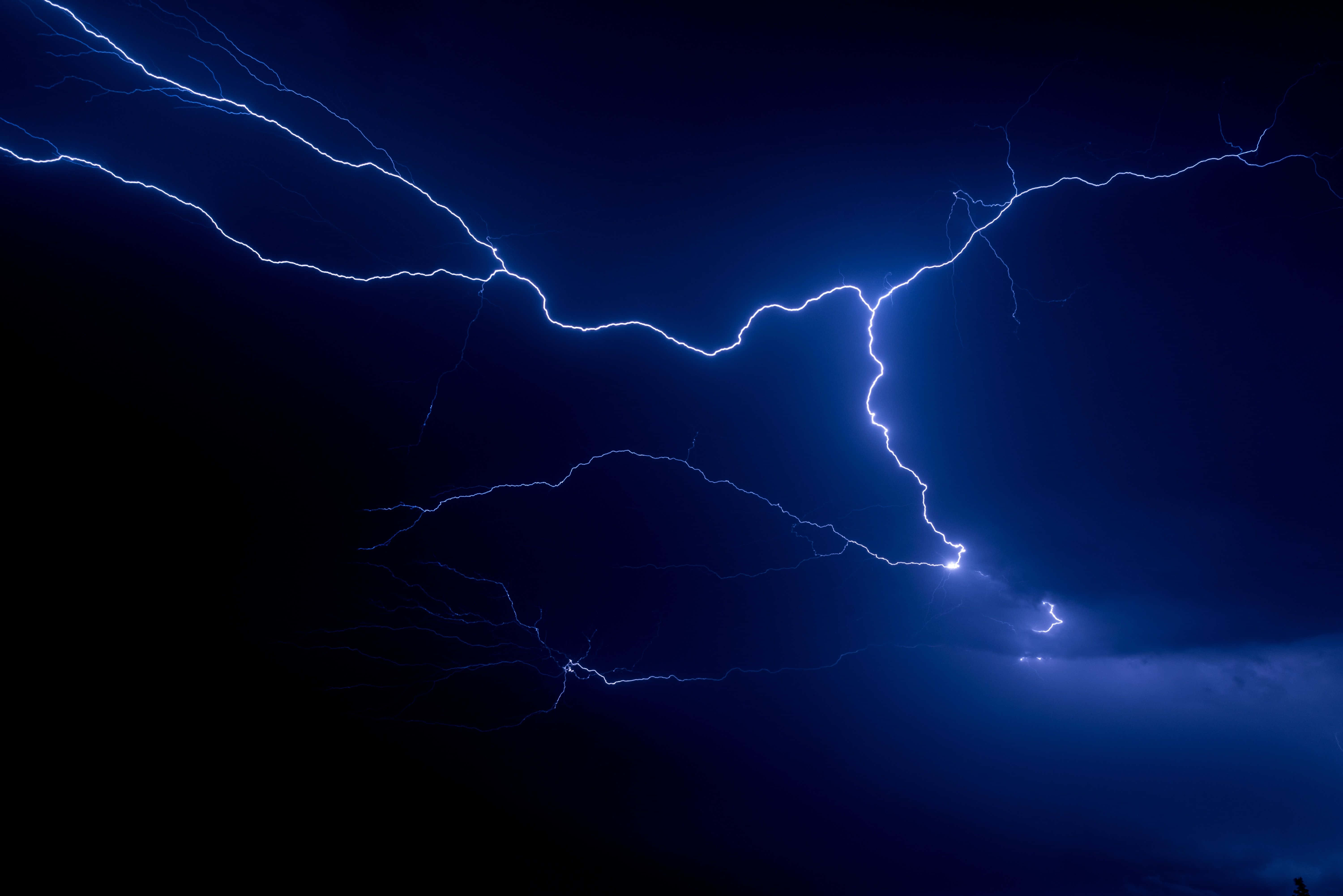 Thunderstorm 桌布 壁紙 — 一道強勁的藍色閃電在深靛藍色的暴風雨天空中分叉，以電能照亮旋轉的雲層。