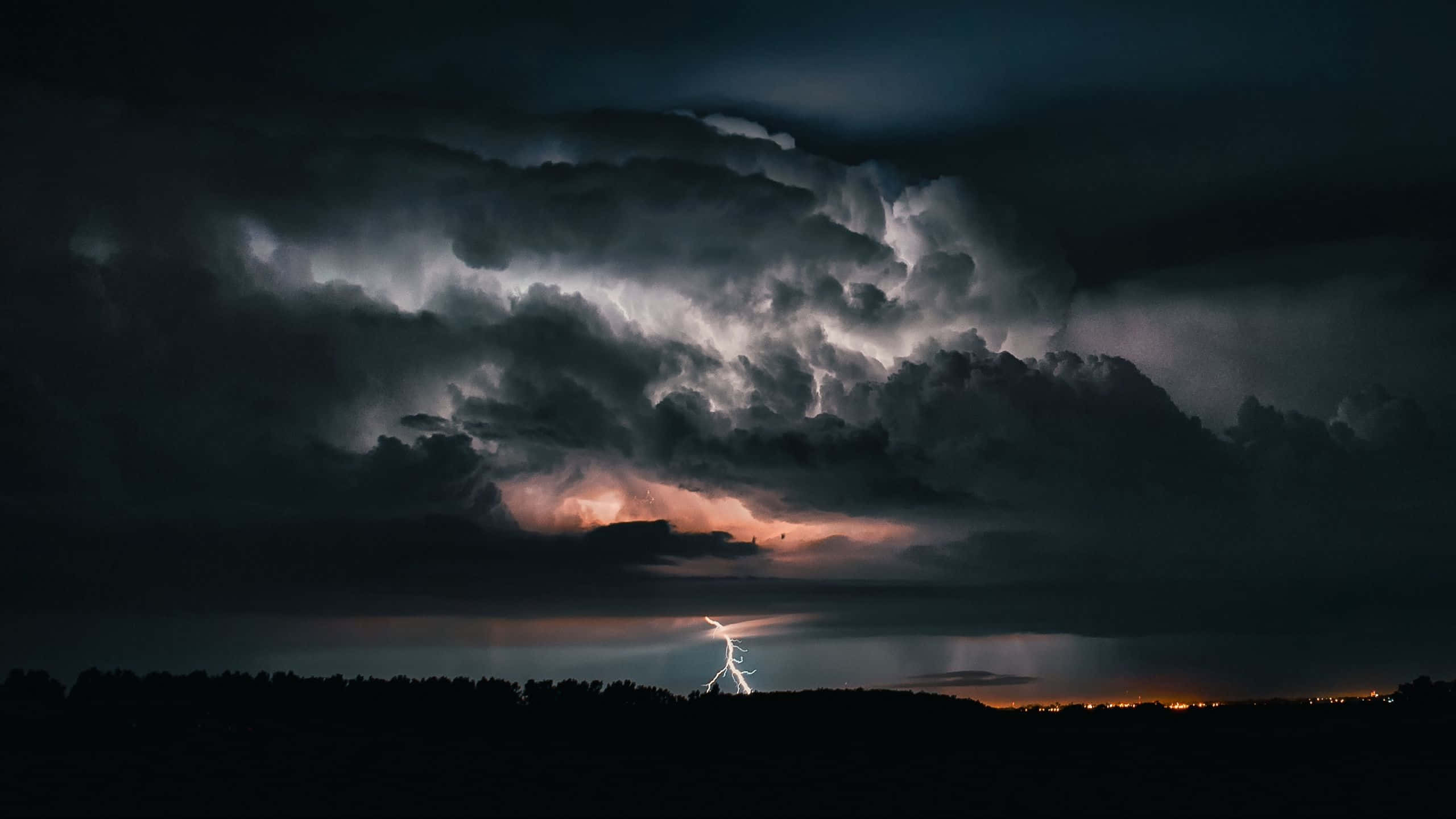 Thunderstorm 桌布 壁紙 — 一道戲劇性的閃電劃破高聳的暴風雲，照亮了夜晚黑暗森林的輪廓。