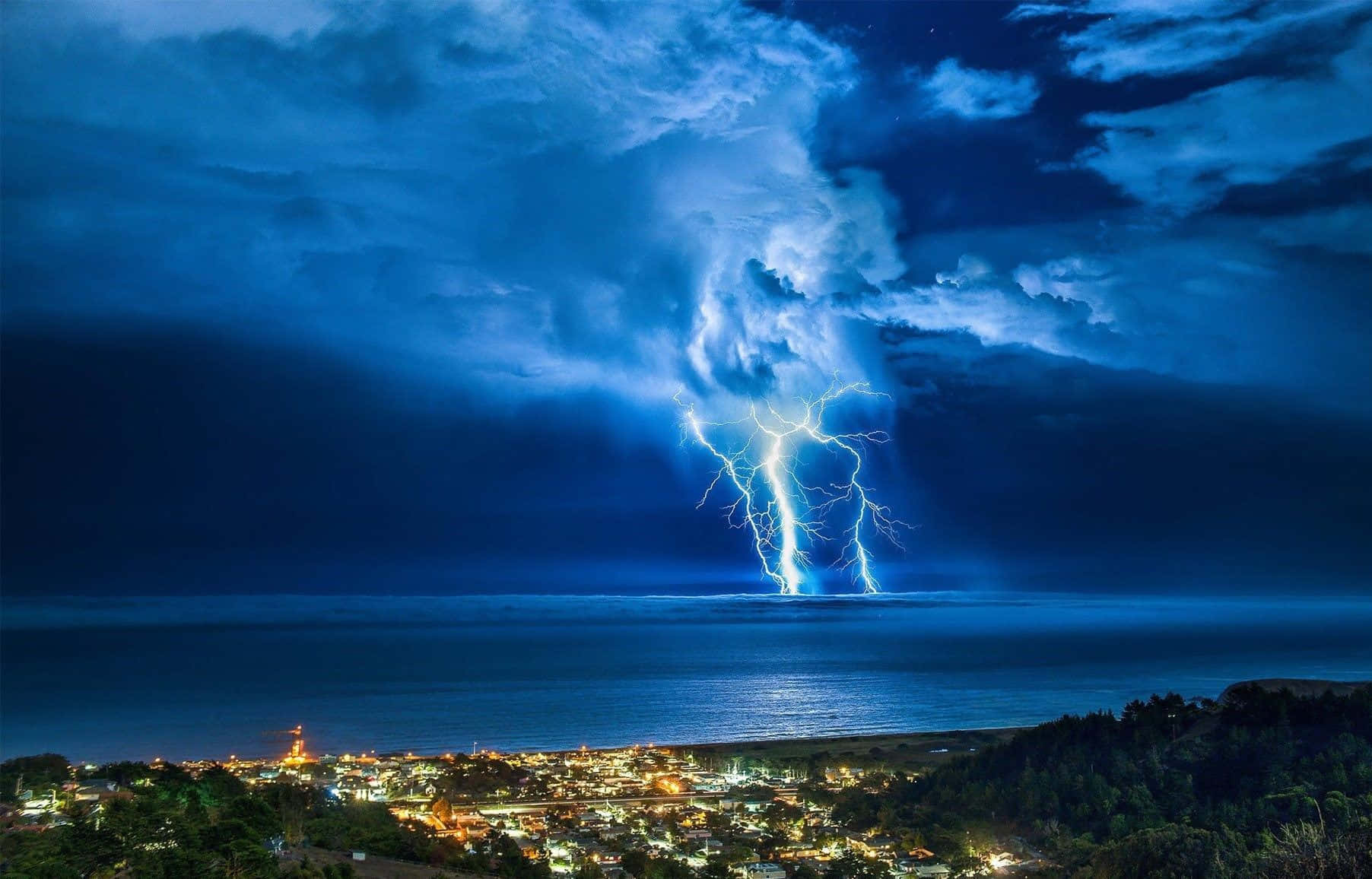 thunder 桌布 壁紙 — 一道戲劇性的閃電劃過黑暗的海洋，下方的沿海小鎮閃爍著溫暖的燈光。