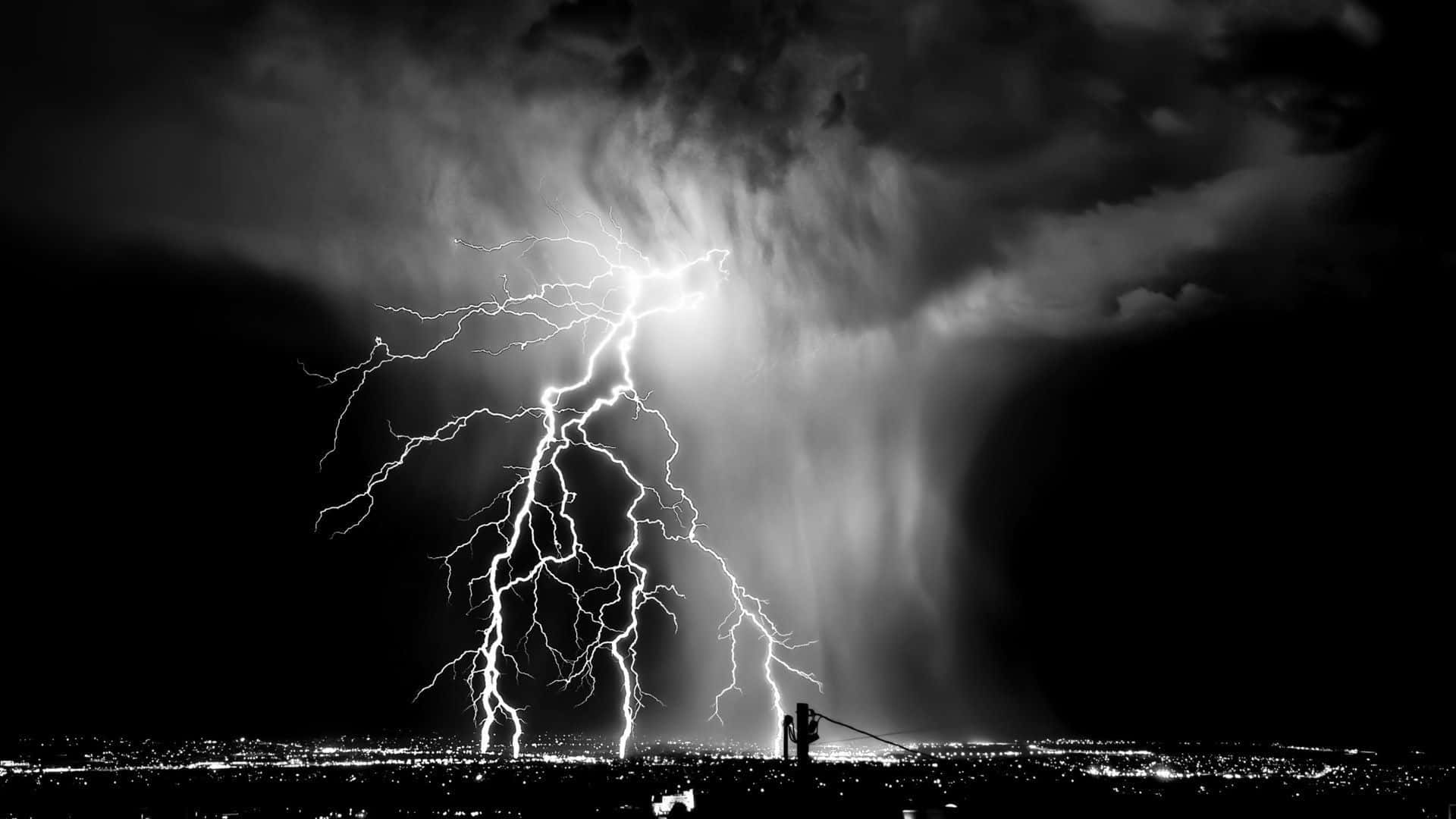 暴風 桌布 壁紙 — 一道戲劇性的黑白閃電照亮了暴風雨夜晚的天空，下方是廣闊的城市景觀，遠處燈光閃爍。