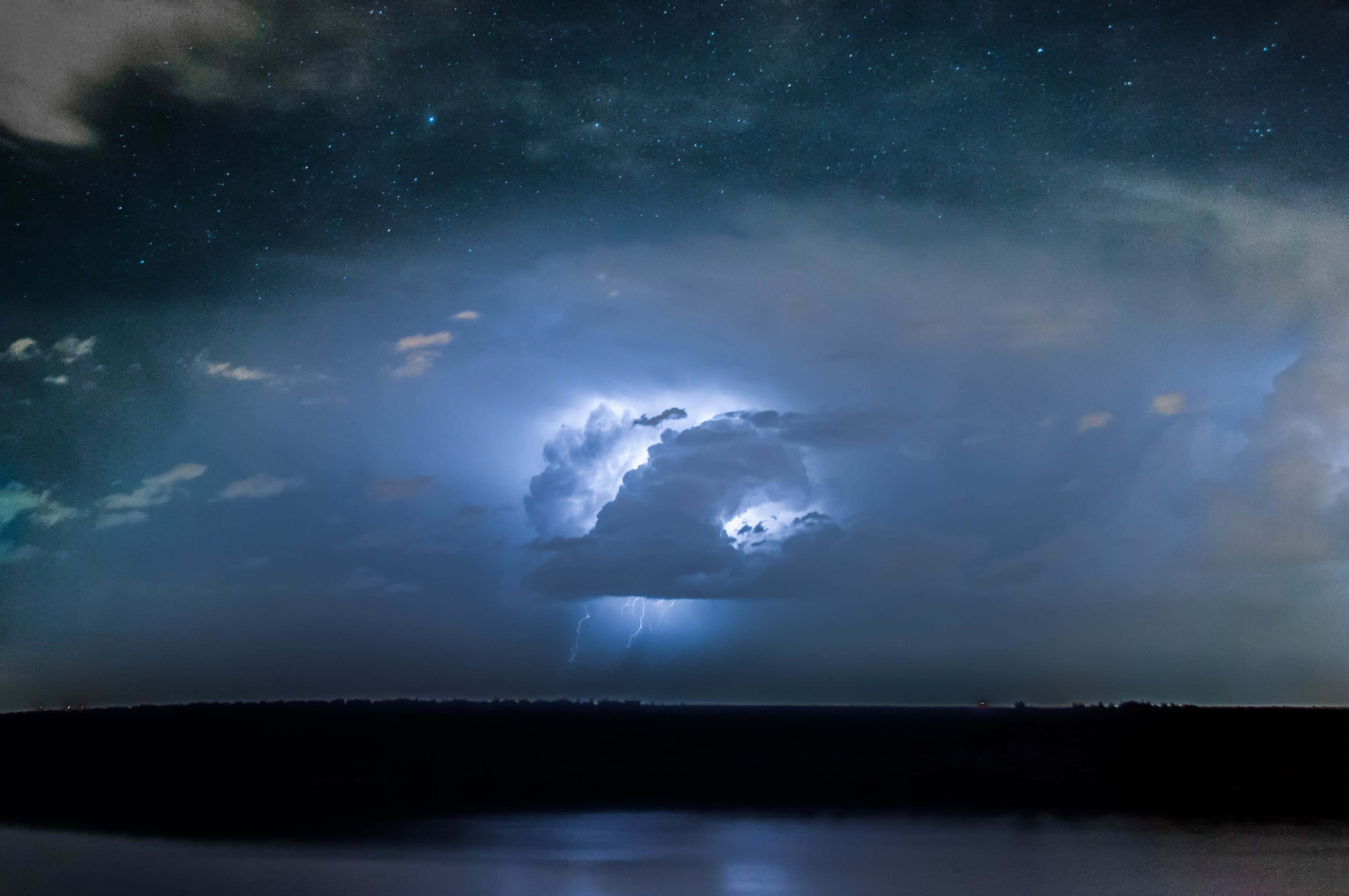 暴風 桌布 壁紙 — 一道明亮的閃電照亮了黑暗湖泊上空暴風雲，背景是繁星點點的夜空。
