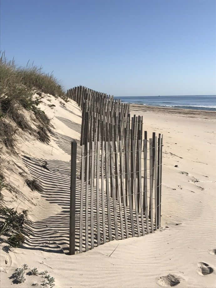 Winter Beach 桌布 壁紙 — 一道木柵欄沿著沙丘延伸，遠方是湛藍天空下的海浪。