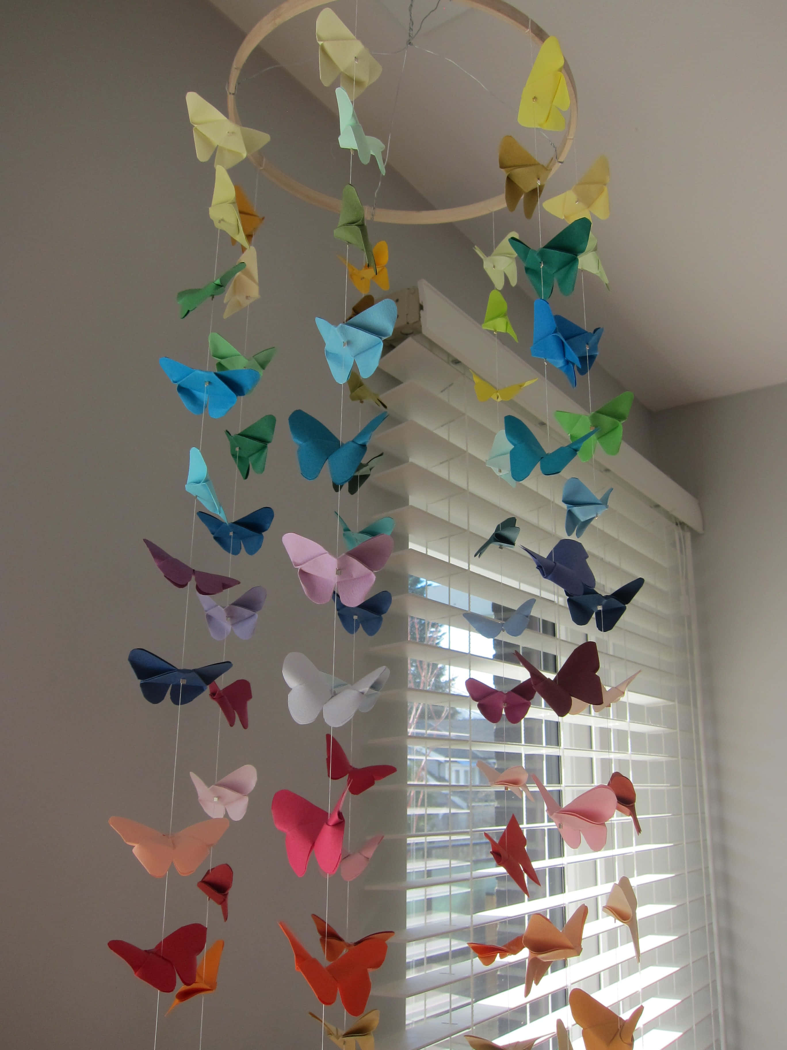 Butterfly Origami 桌布 壁紙 — 一道色彩繽紛的紙蝴蝶彩虹掛在窗邊的木環上，窗戶裝有百葉簾。