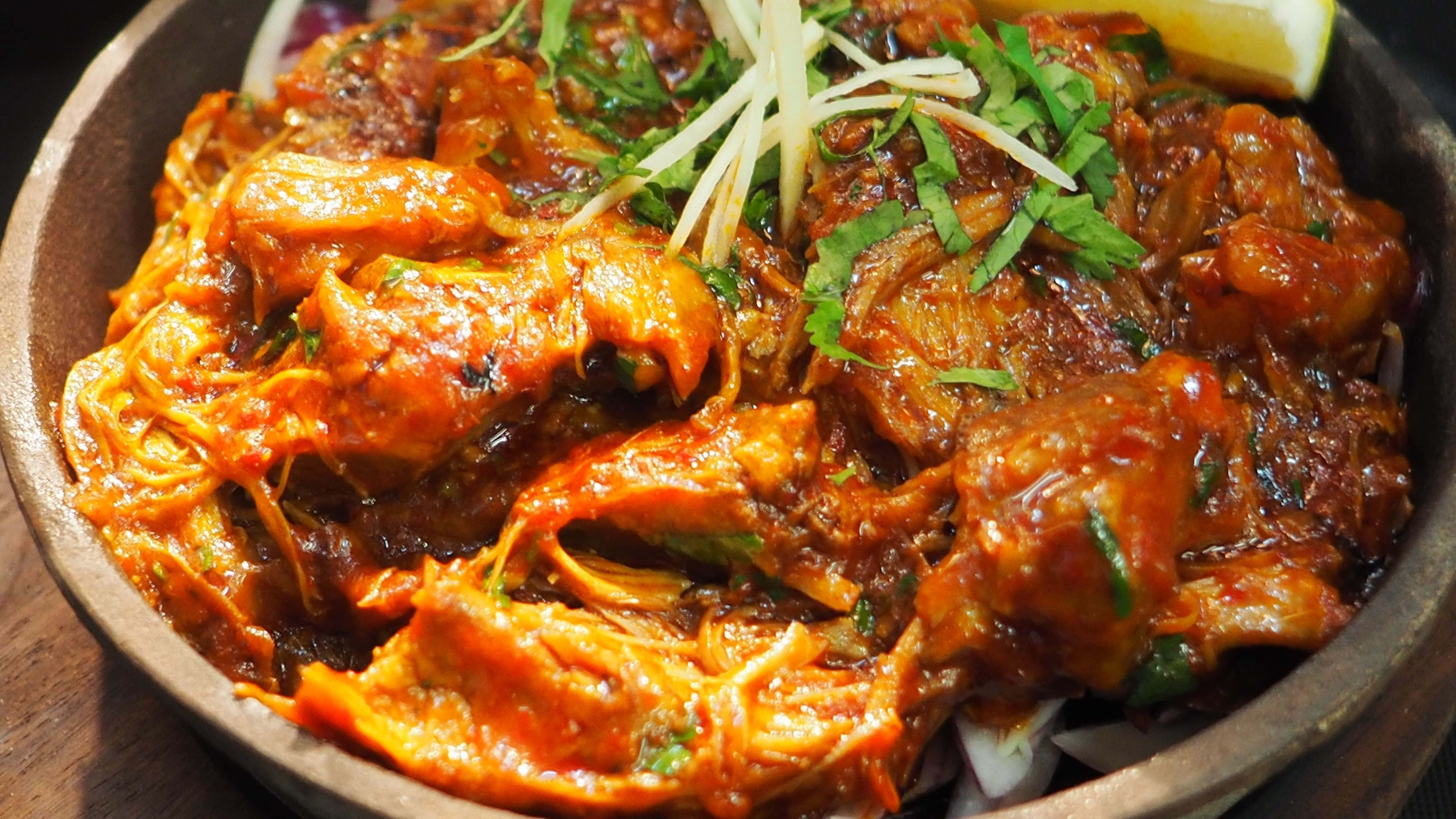 Indian Food 桌布 壁紙 — 一道醬汁濃郁的雞肉菜餚，飾以新鮮香草和檸檬角，誘人地放在一個質樸的木碗中。