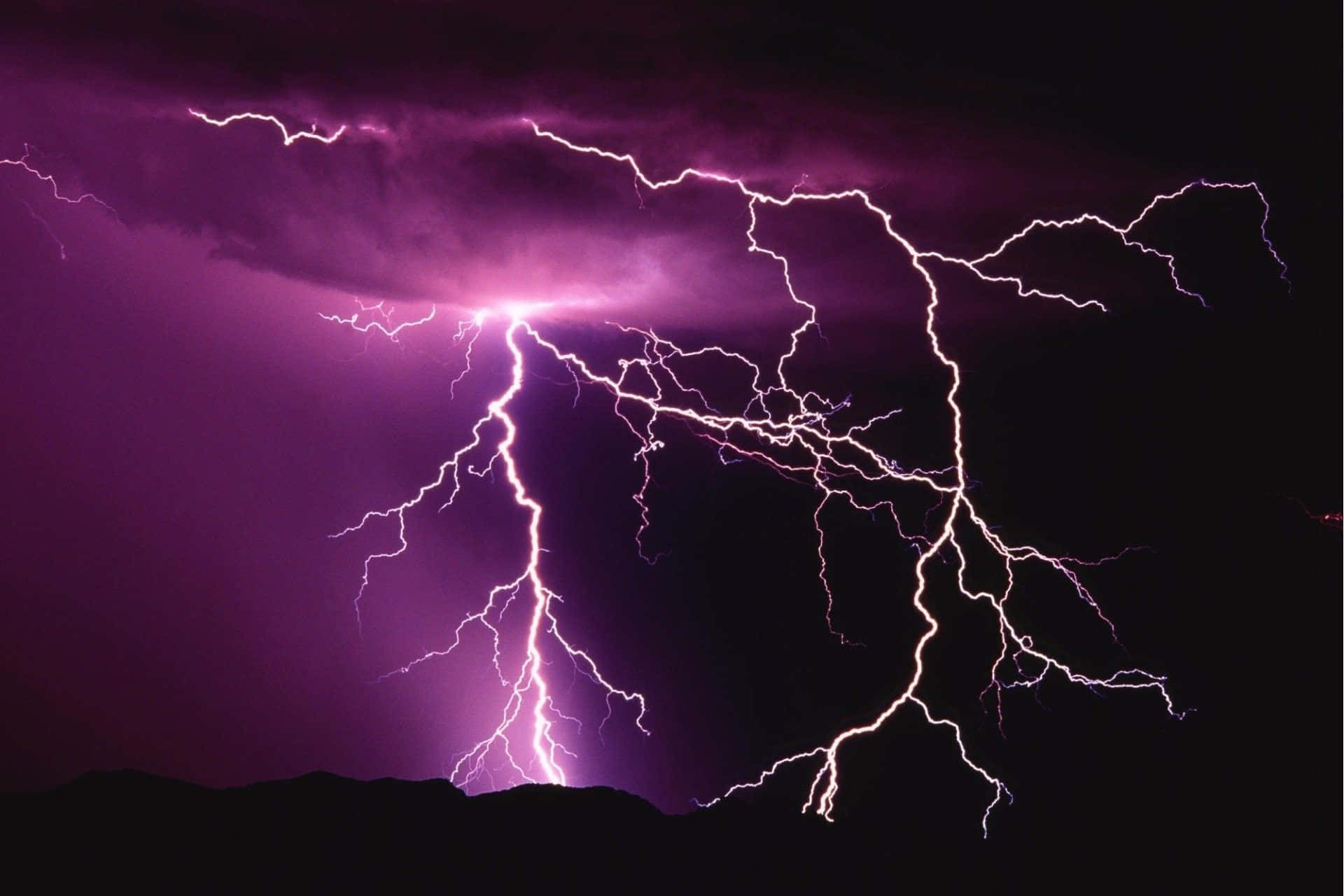 一道閃電照亮陰沉的雷暴雲 壁紙 — 一場戲劇性的紫色閃電風暴照亮了鋸齒狀山脈輪廓上方的黑暗天空。
