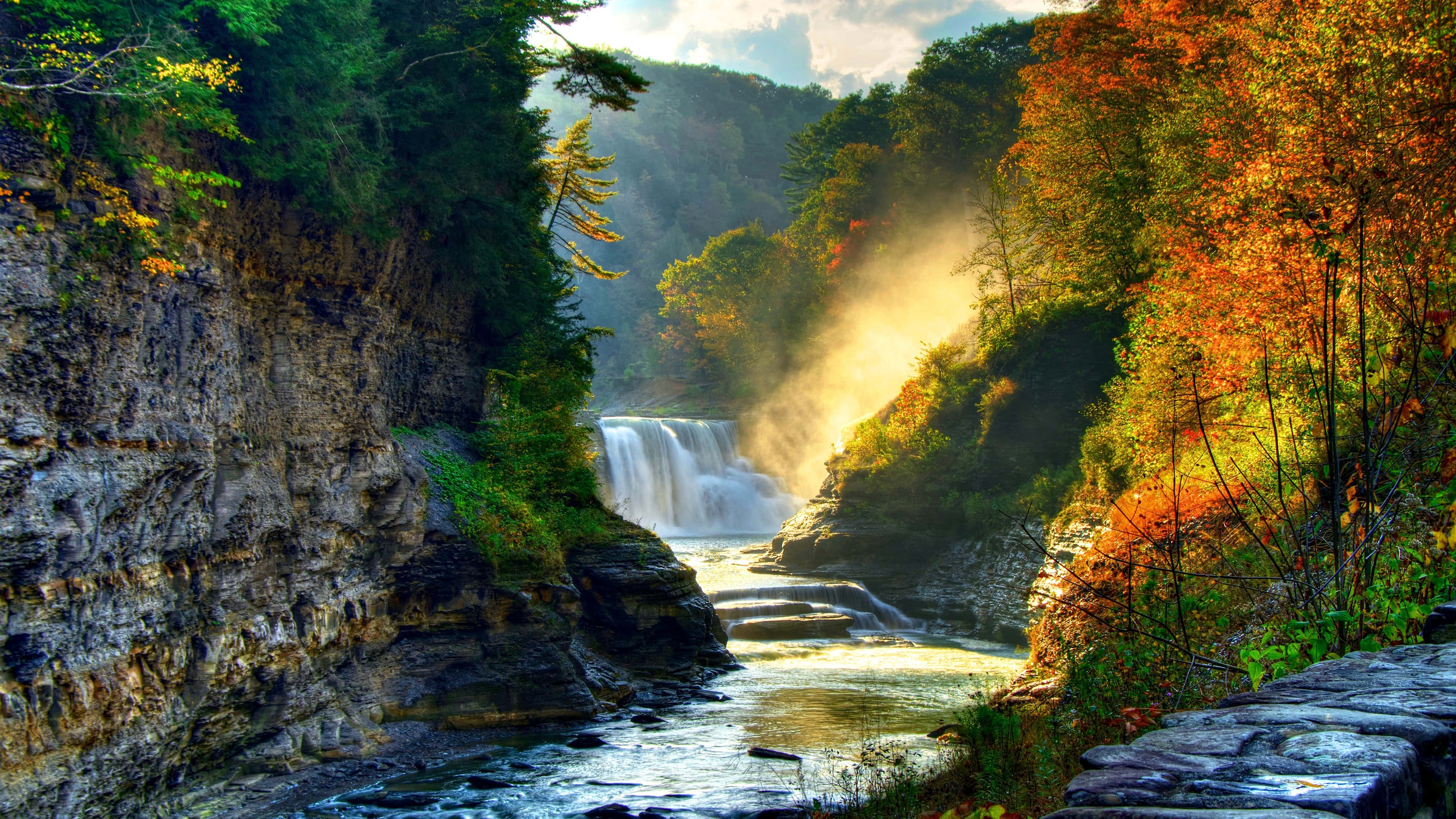 Nature Scenery 桌布 壁紙 — 一道雄偉的瀑布穿過充滿活力的秋日森林，金色的光線透過色彩繽紛的樹木灑落。