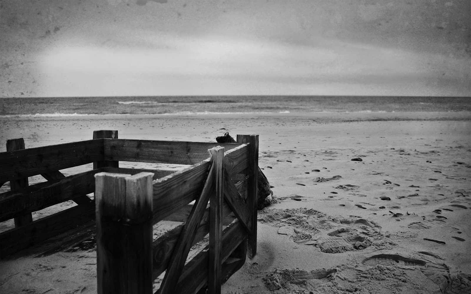 Black And White Landscape 桌布 壁紙 — 一道風化的木柵欄框住了一個荒涼的海灘，天空多雲，沙灘上有腳印。