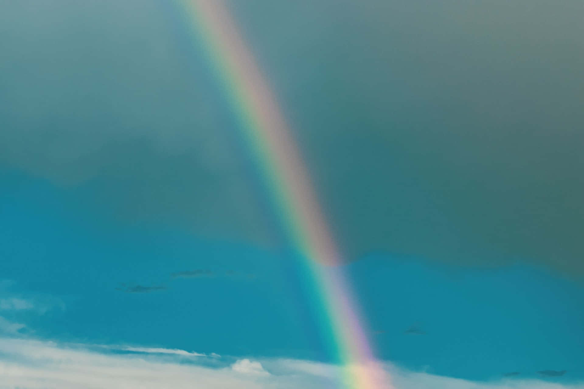 Bifrost 桌布 壁紙 — 一道鮮豔的彩虹劃過戲劇性的天空，天空在暴風雨的灰色雲層和明亮的藍色區域之間分裂。