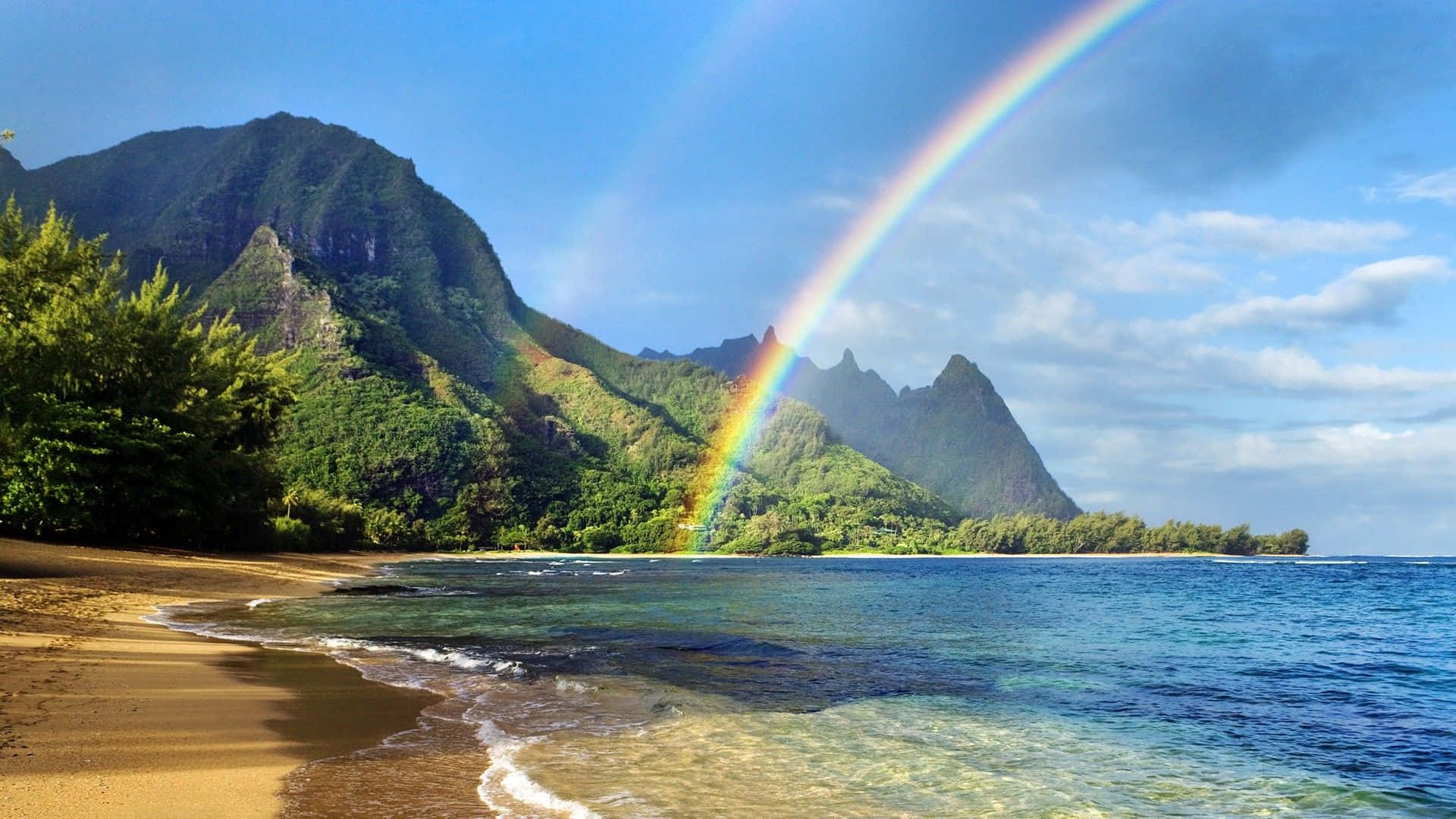 Hawaiian Beach 桌布 壁紙 — 一道鮮豔的彩虹橫跨在熱帶海灘上，碧綠的海水、茂密的青山，在明亮的藍天下格外動人。