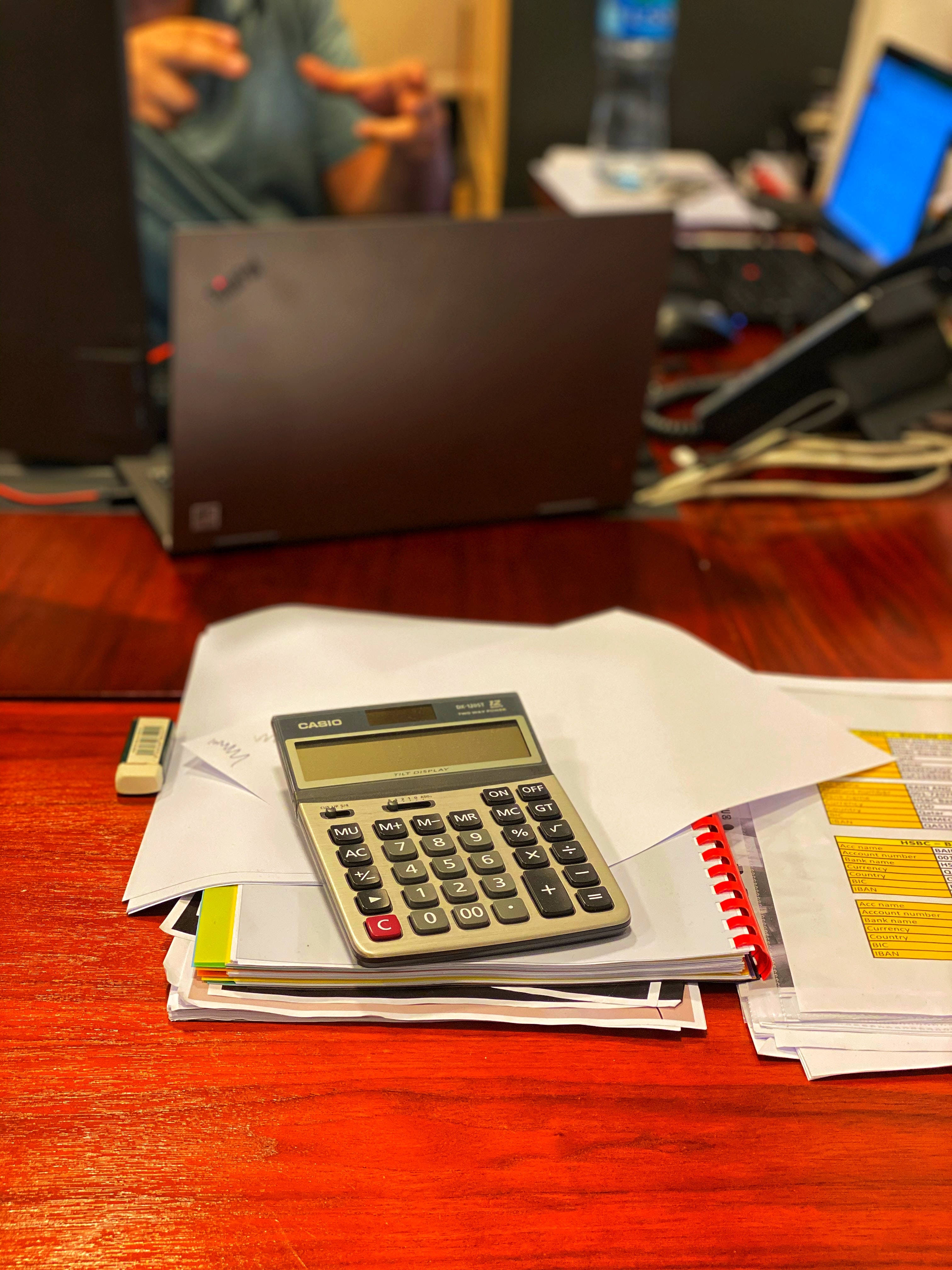 Chartered Accountant 桌布 壁紙 — 一部 Casio 計算機放在一個雜亂辦公室中拋光木桌上的一疊文件和紅色線圈筆記本上。