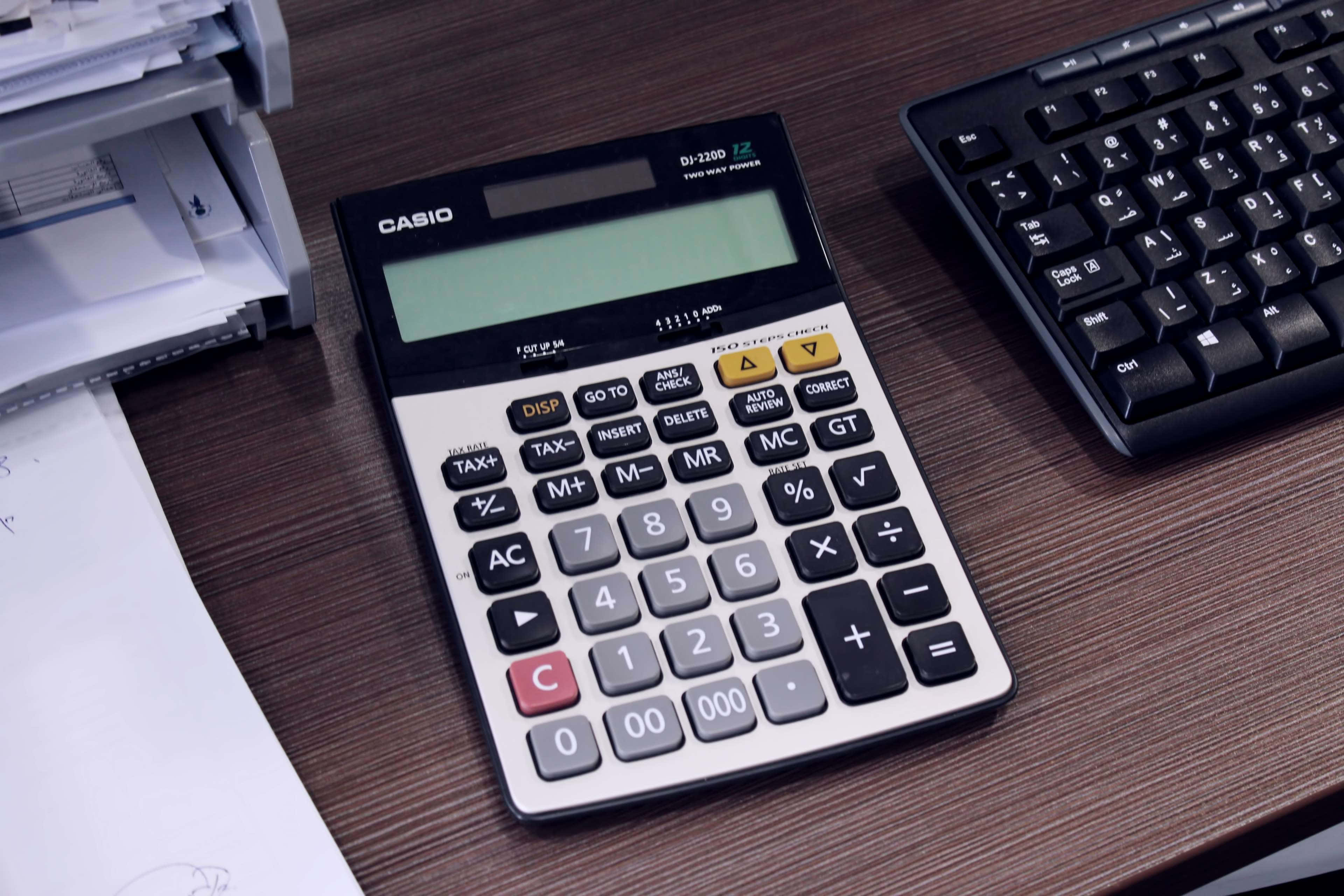 Calculator 桌布 壁紙 — 一部 Casio 計算機放在木桌中央，旁邊有鍵盤和打印機（附紙張）。