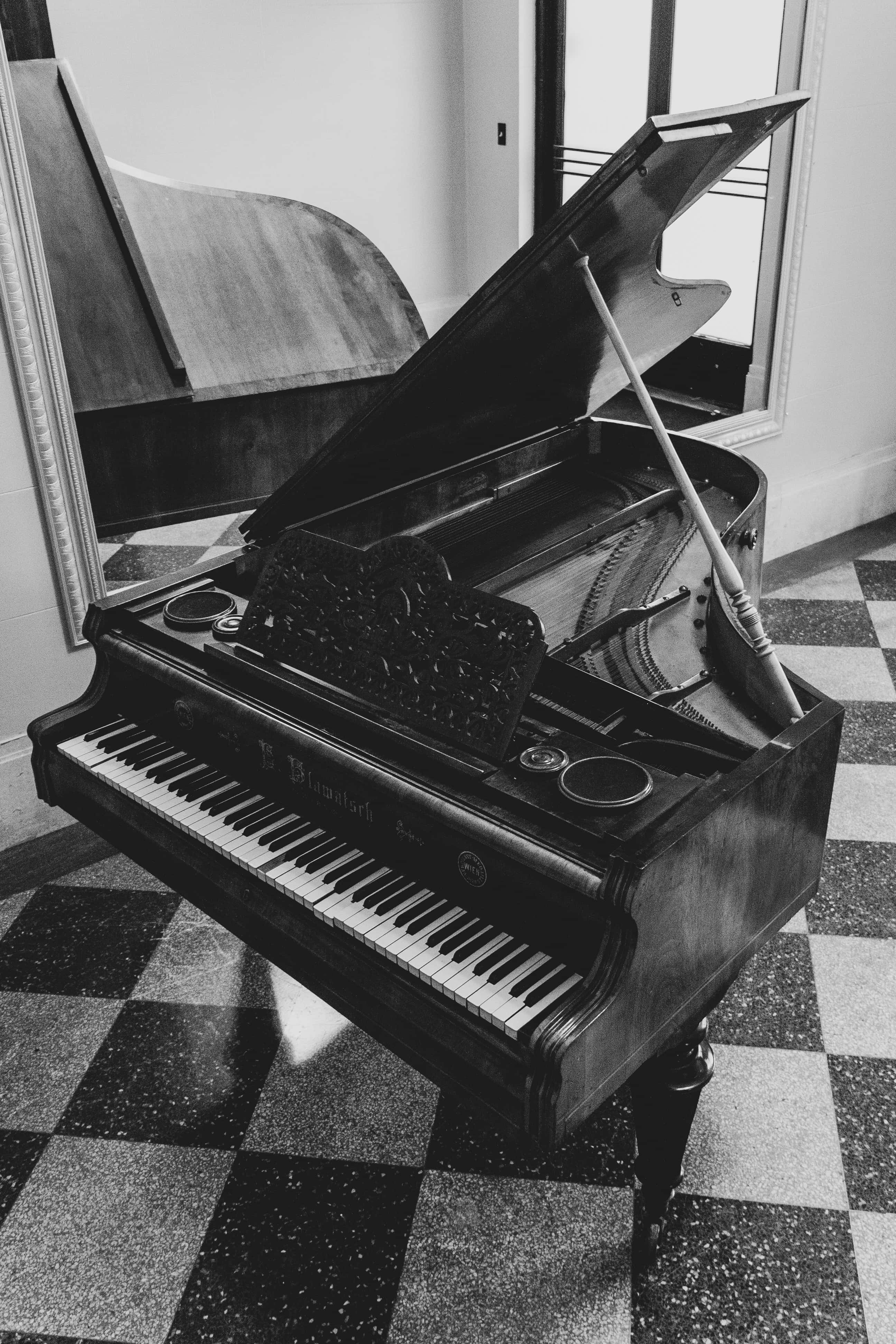 Black And White Piano 桌布 壁紙 — 一部三角鋼琴打開蓋子，放在單色房間的棋盤格地板上，房間有窗戶的自然光。