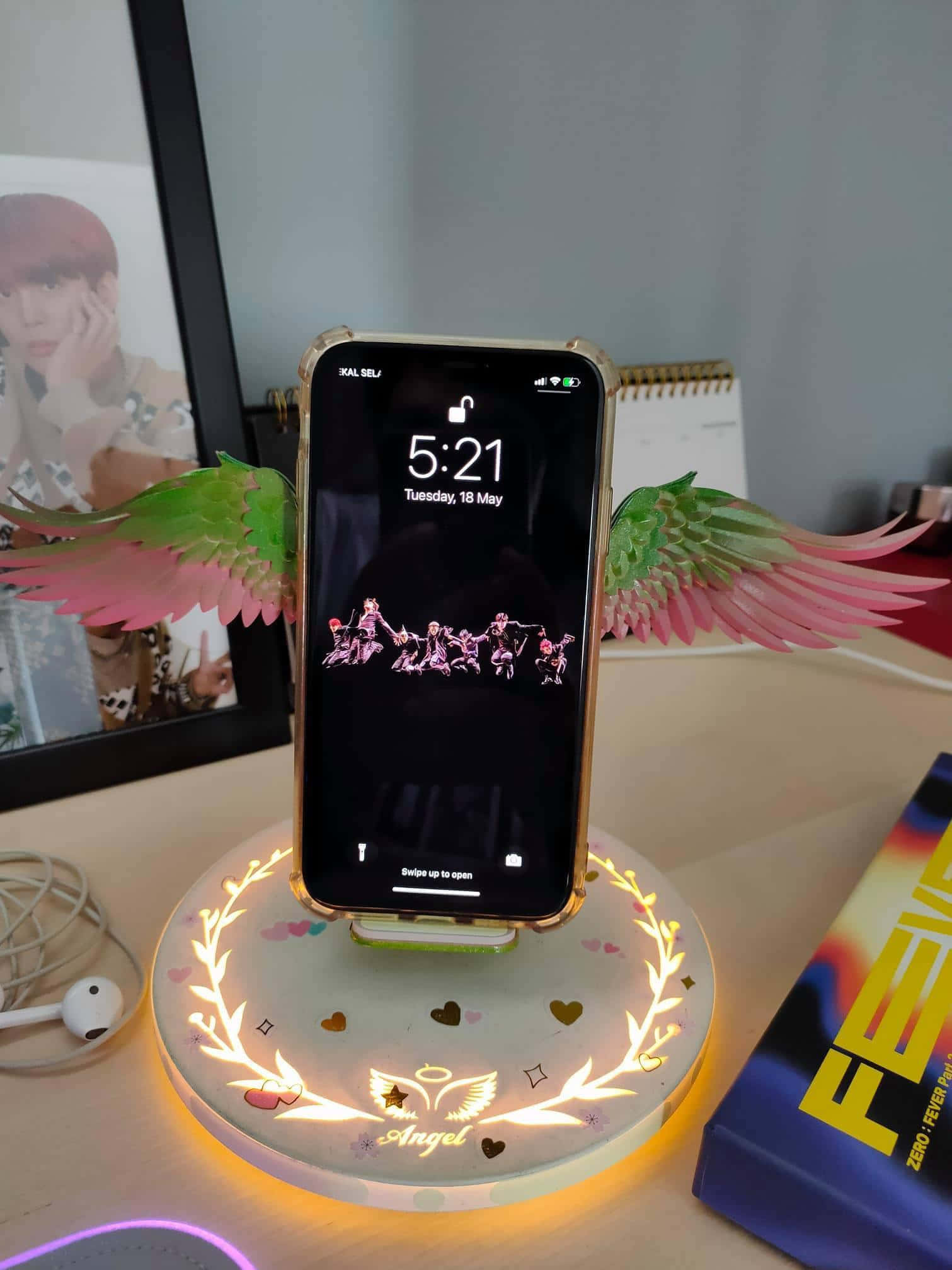 Wireless Charging 桌布 壁紙 — 一部帶有天使翅膀和發光底座嘅智能手機放在枱上，旁邊有一個相框同書。