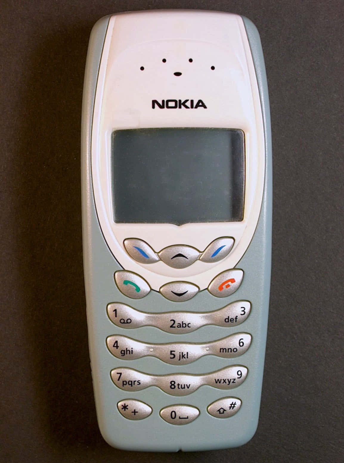 Nokia 桌布 壁紙 — 一部帶有淺藍色和銀色鍵盤的復古Nokia手機放在深灰色表面上。
