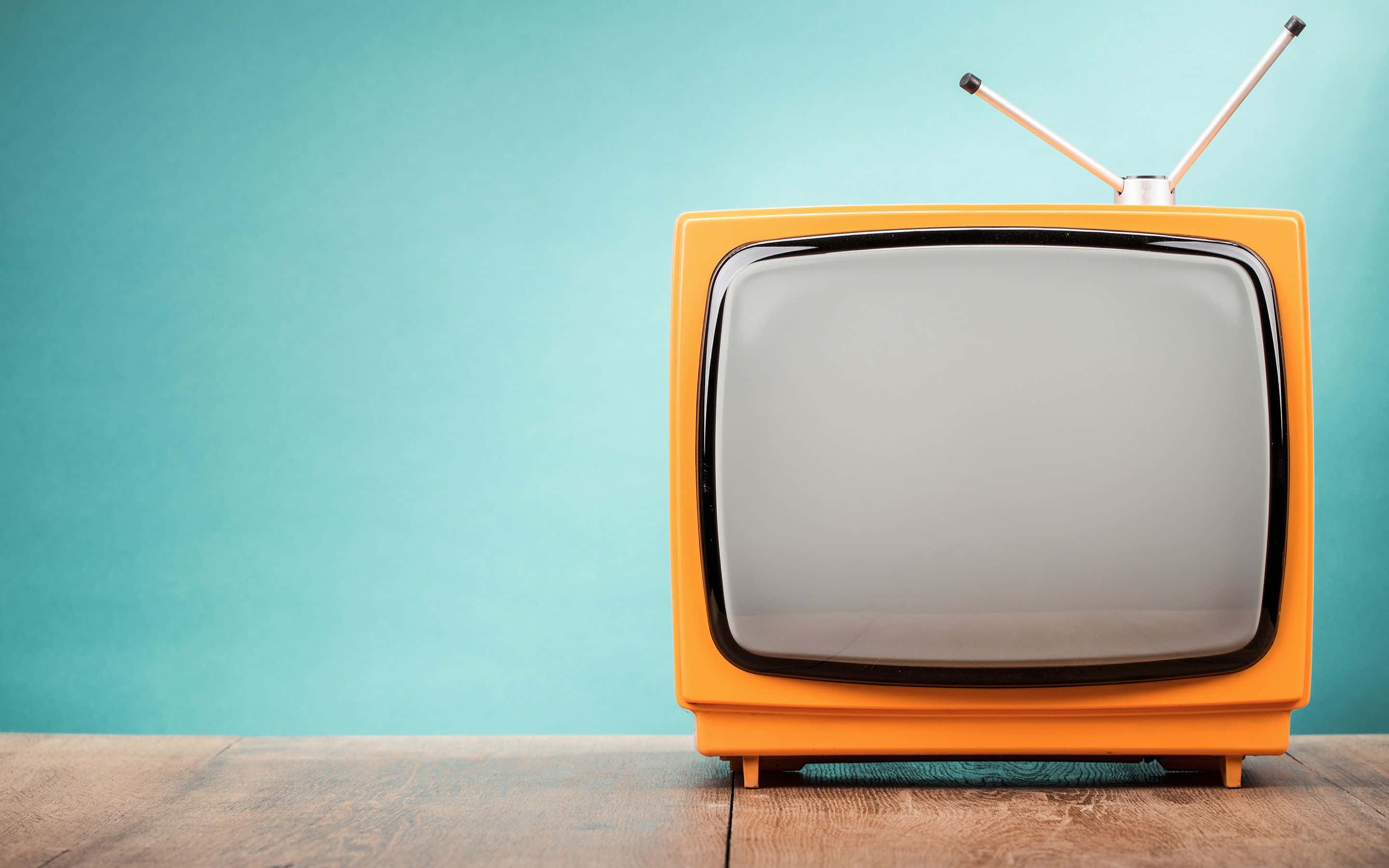 tv 桌布 壁紙 — 一部帶有鍍鉻天線的復古橙色電視機放在木質表面上，背景是青綠色牆壁。