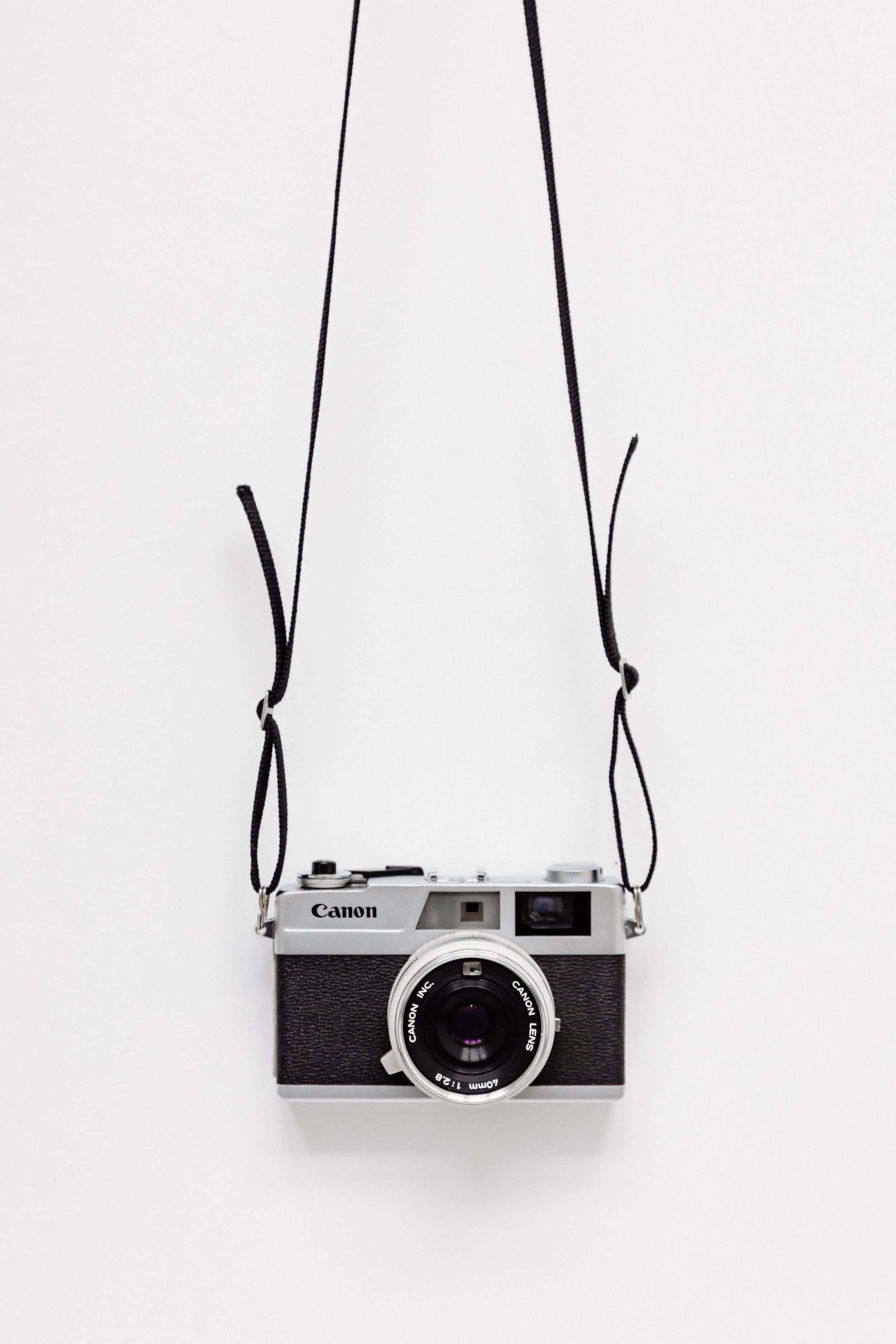 Minimalist Photography 桌布 壁紙 — 一部復古 Canon 菲林相機用黑色掛帶掛在純白背景上。