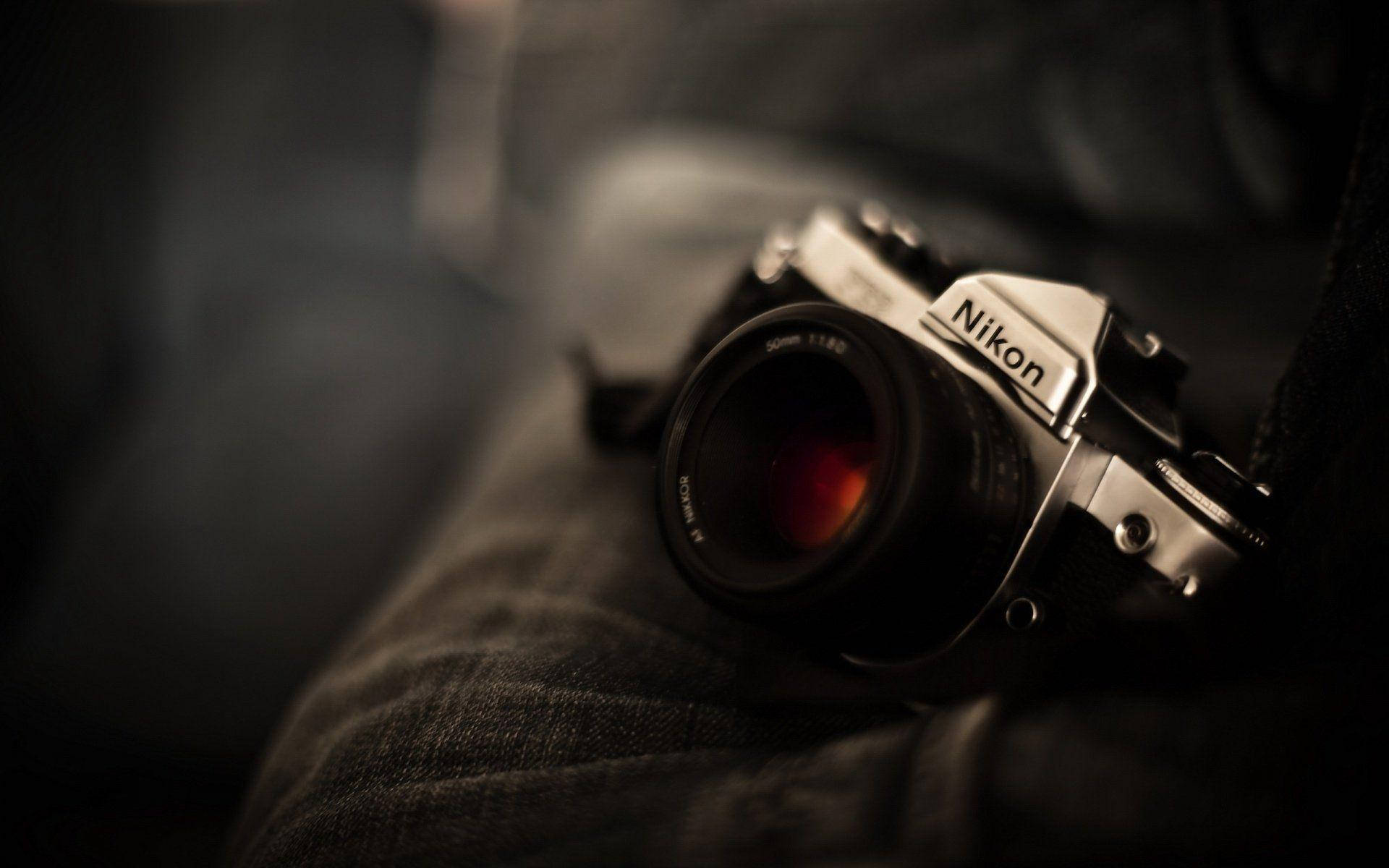 相機 桌布 壁紙 — 一部復古Nikon菲林相機放置在深色牛仔布上，景深淺，帶有溫暖的電影感燈光。