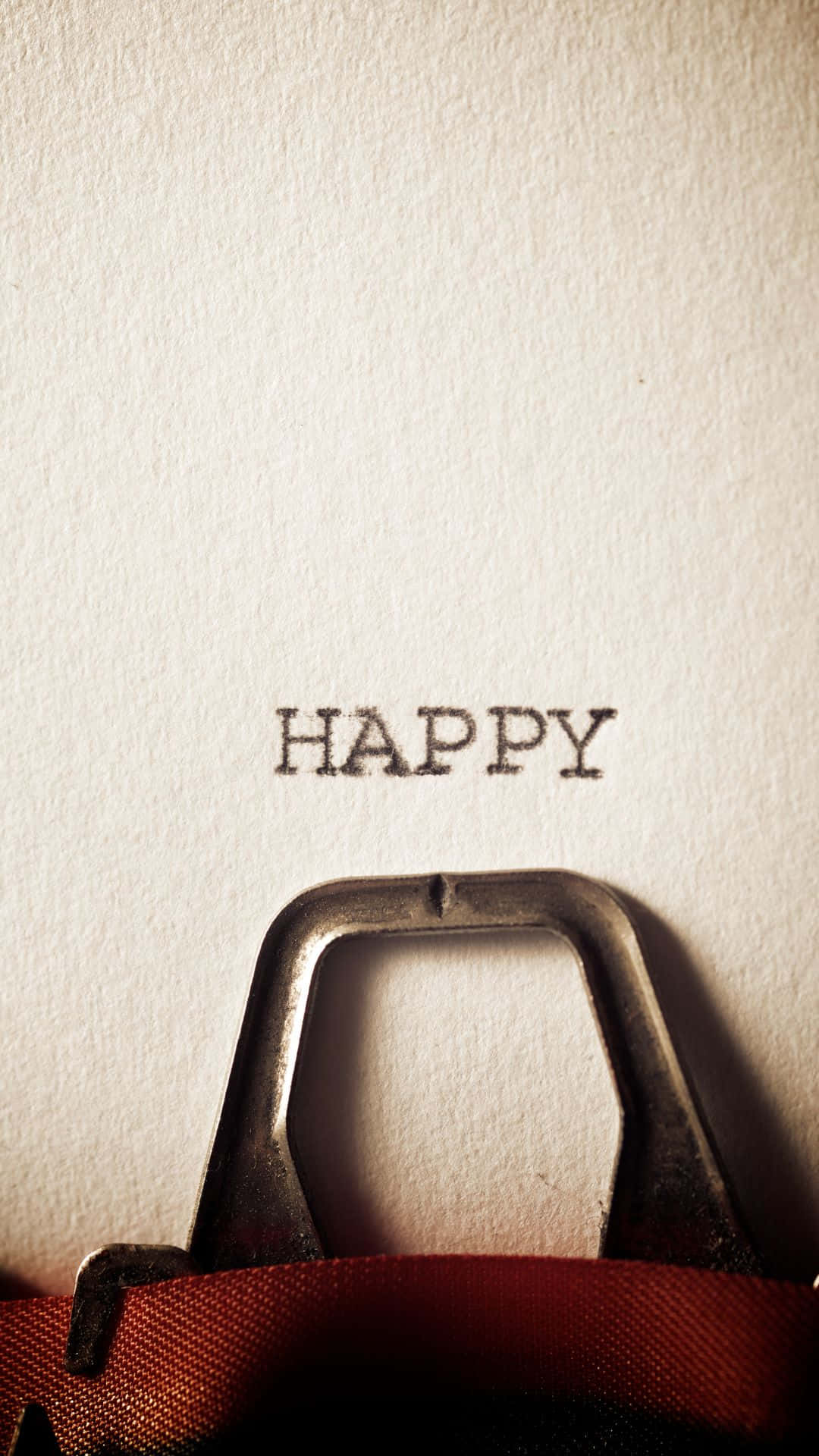 Happy iPhone 桌布 壁紙 — 一部復古打字機的按鍵在溫暖燈光下將「happy」一詞壓印在帶紋理的奶油色紙上。
