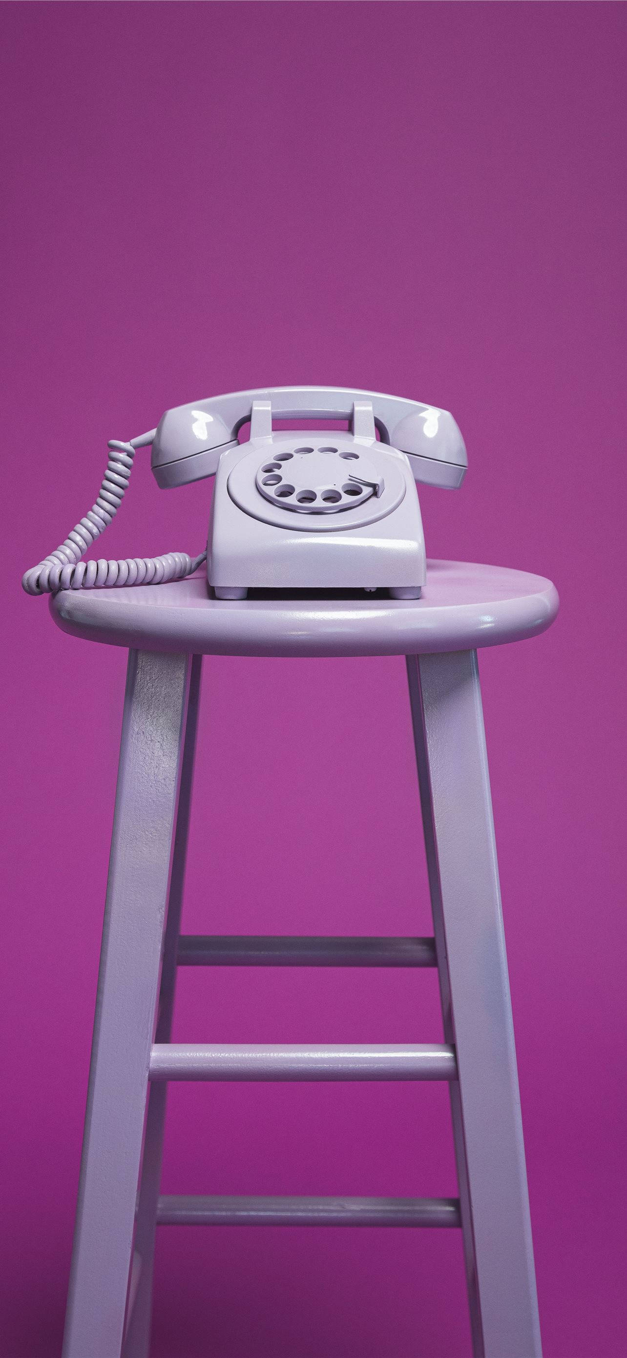 retro aesthetic iPhone 桌布 壁紙 — 一部復古白色轉盤電話放在相配的凳子上，背景為純紫色。