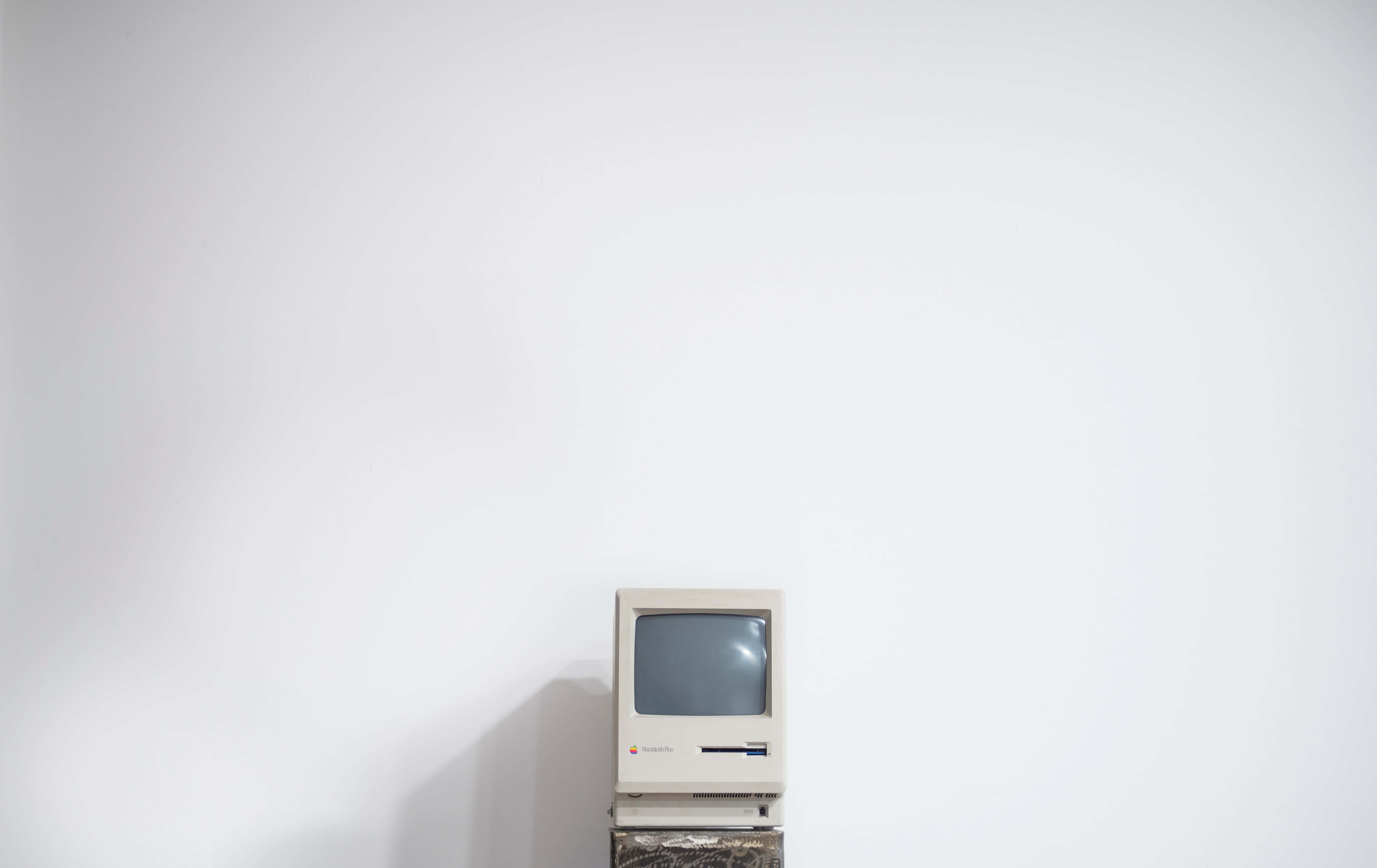 Minimalist Vintage 桌布 壁紙 — 一部復古米色 Apple Macintosh 電腦獨自放在木製支架上，背景是純白牆壁。