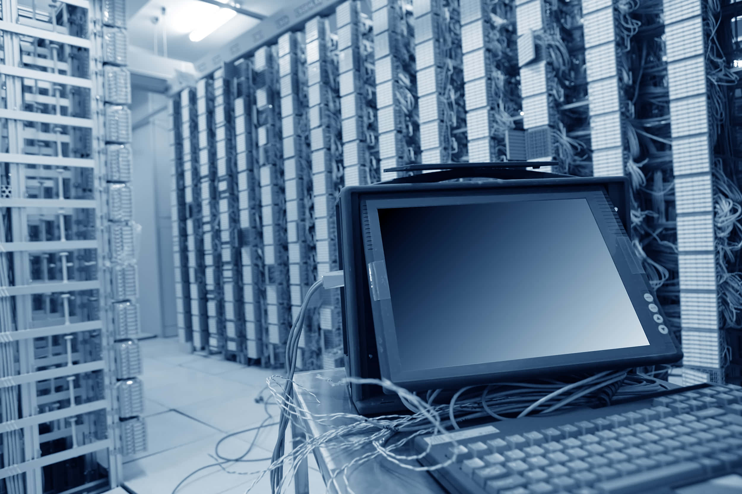 Data Management 桌布 壁紙 — 一部復古電腦終端機放置在冷色調藍色數據中心的高聳伺服器機架之間。