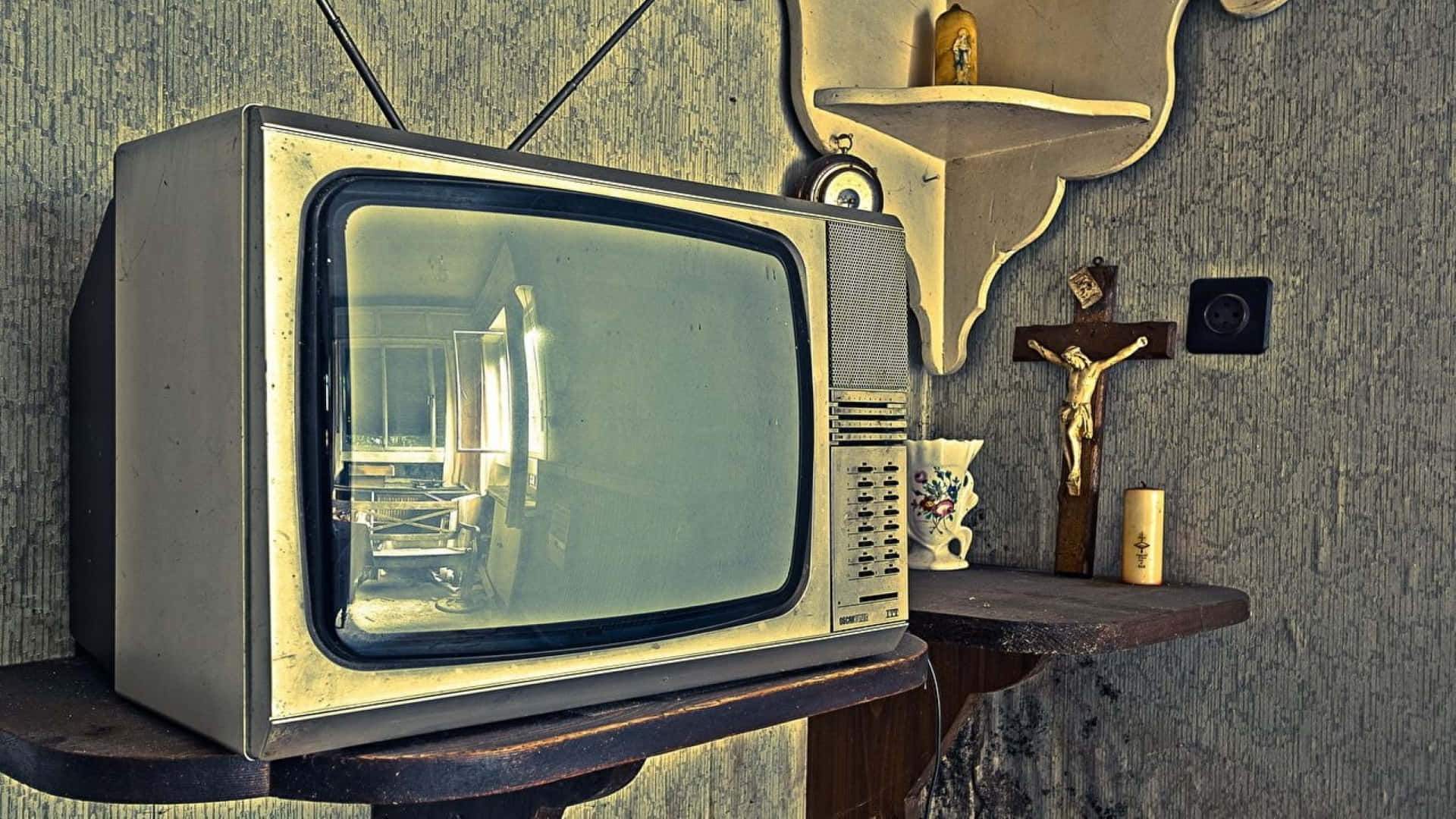 Television Set 桌布 壁紙 — 一部復古電視機放在木架上，旁邊有十字架和蠟燭，房間牆壁有紋理。