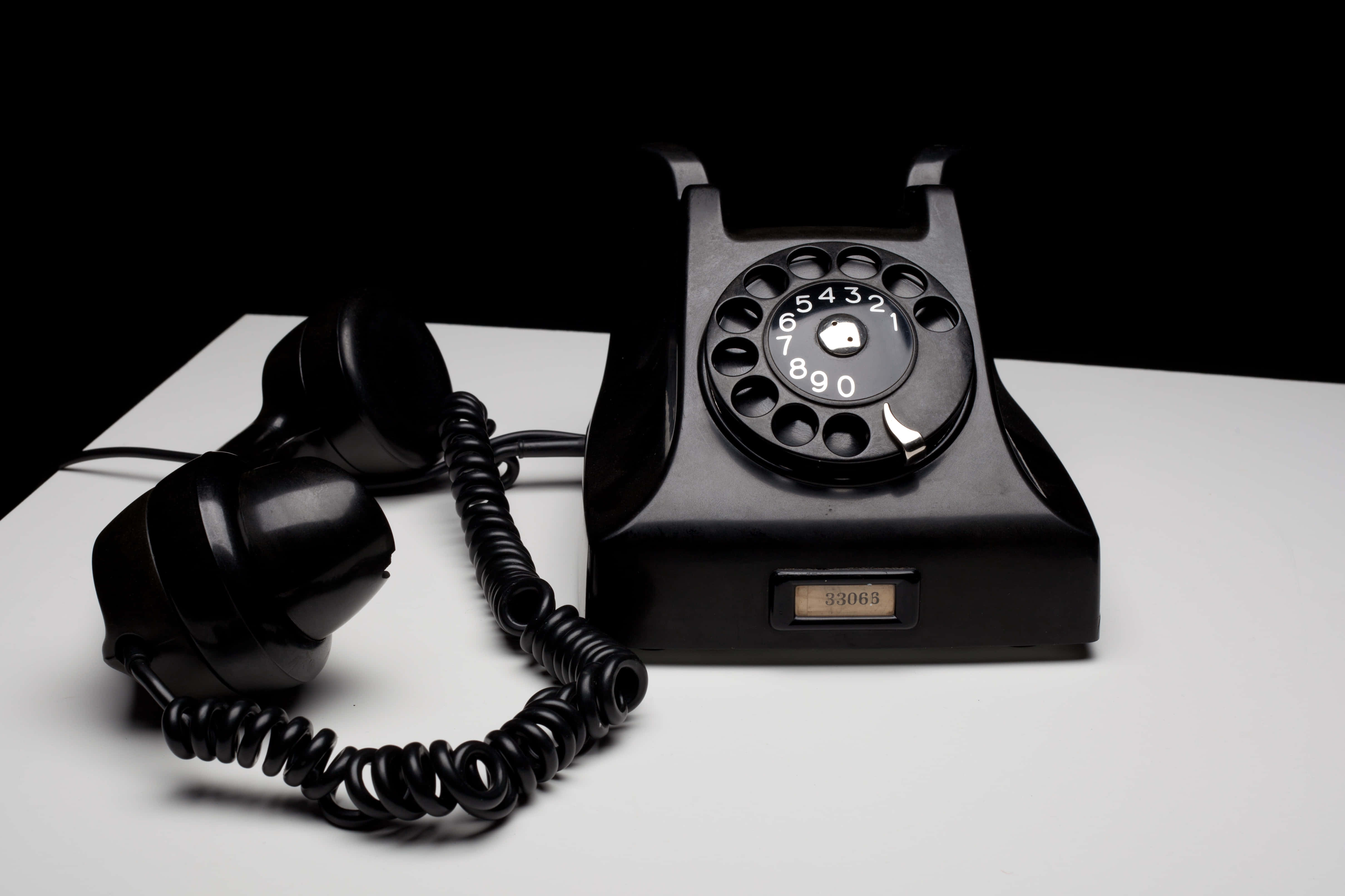 Phone Call 桌布 壁紙 — 一部復古黑色轉盤電話，帶螺旋電線，放在白色表面上，襯托著純黑背景。