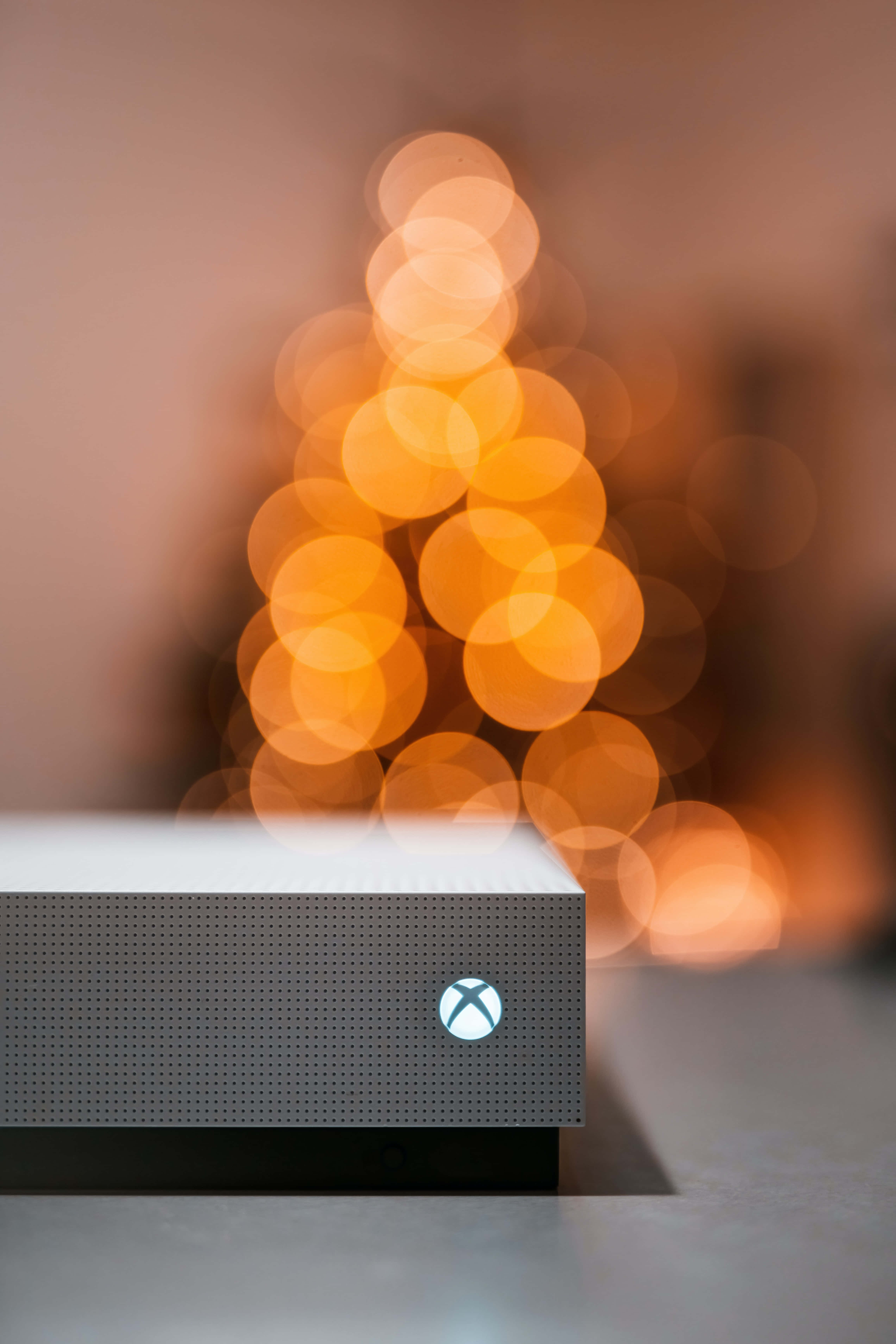 Gaming Consoles 桌布 壁紙 — 一部時尚的Xbox主機位於前景，背後有溫暖的散景聖誕樹柔和地發光。