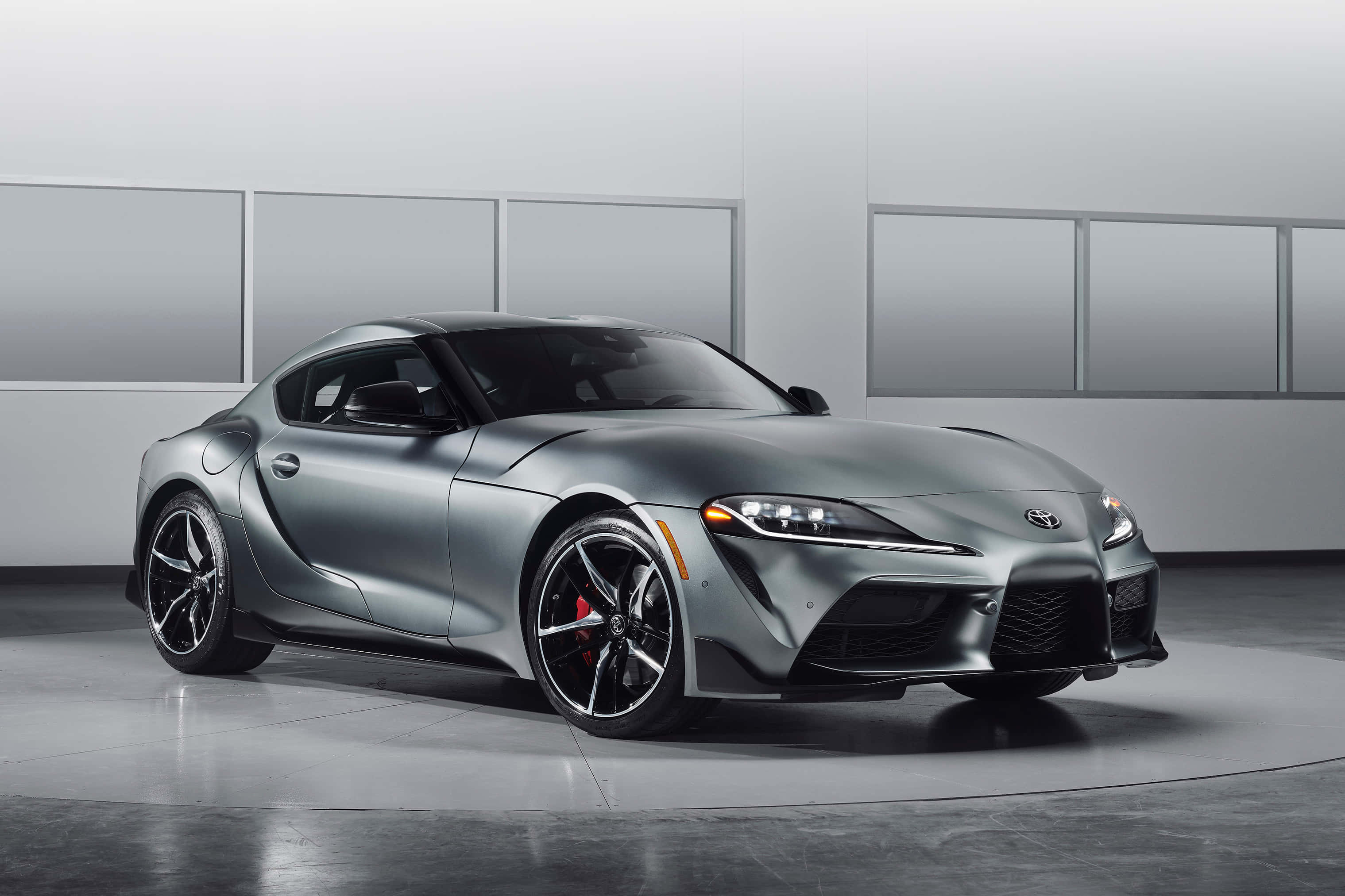 Supra 桌布 壁紙 — 一部時尚的啞光灰色豐田Supra跑車在簡約風格的攝影棚中展示，配有反射地板和柔和燈光。