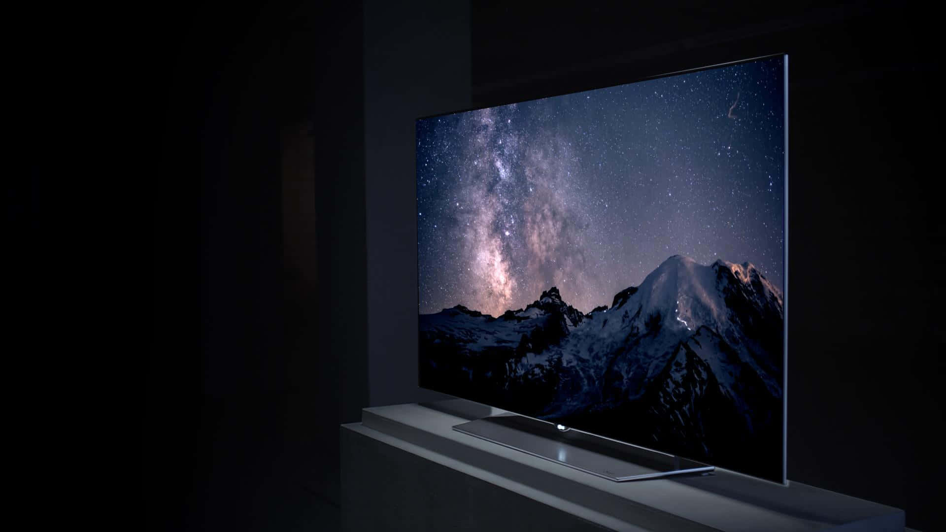 tv 桌布 壁紙 — 一部時尚的現代電視顯示出令人驚嘆的雪山景色，在充滿活力的星空下，銀河系清晰可見。
