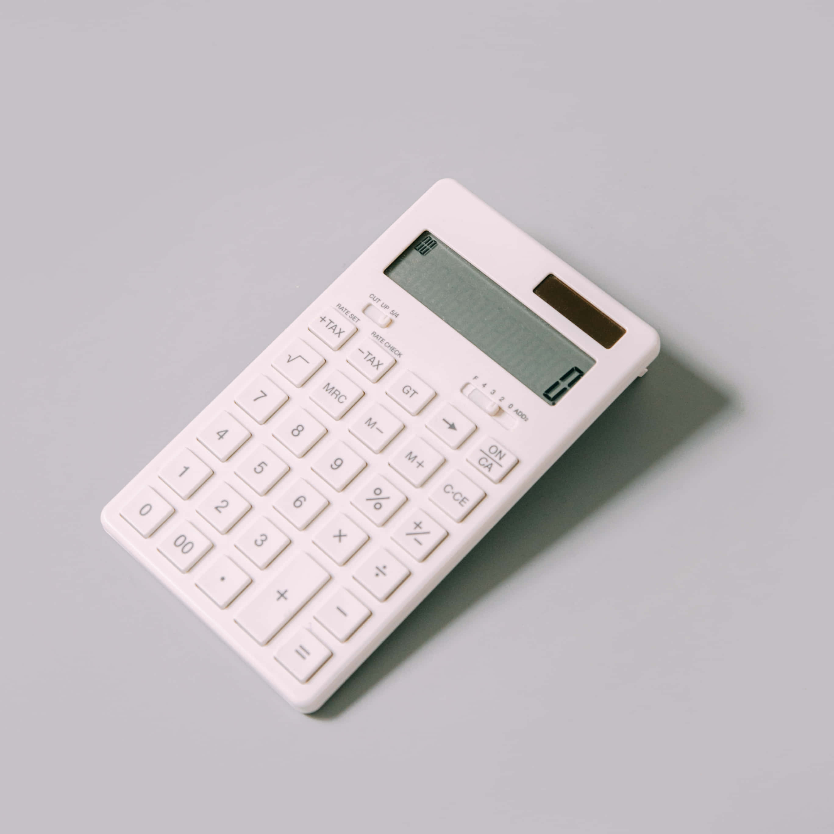 Calculator 桌布 壁紙 — 一部時尚的白色計算器以傾斜角度放置在柔軟的灰色表面上，投射出微妙的陰影。