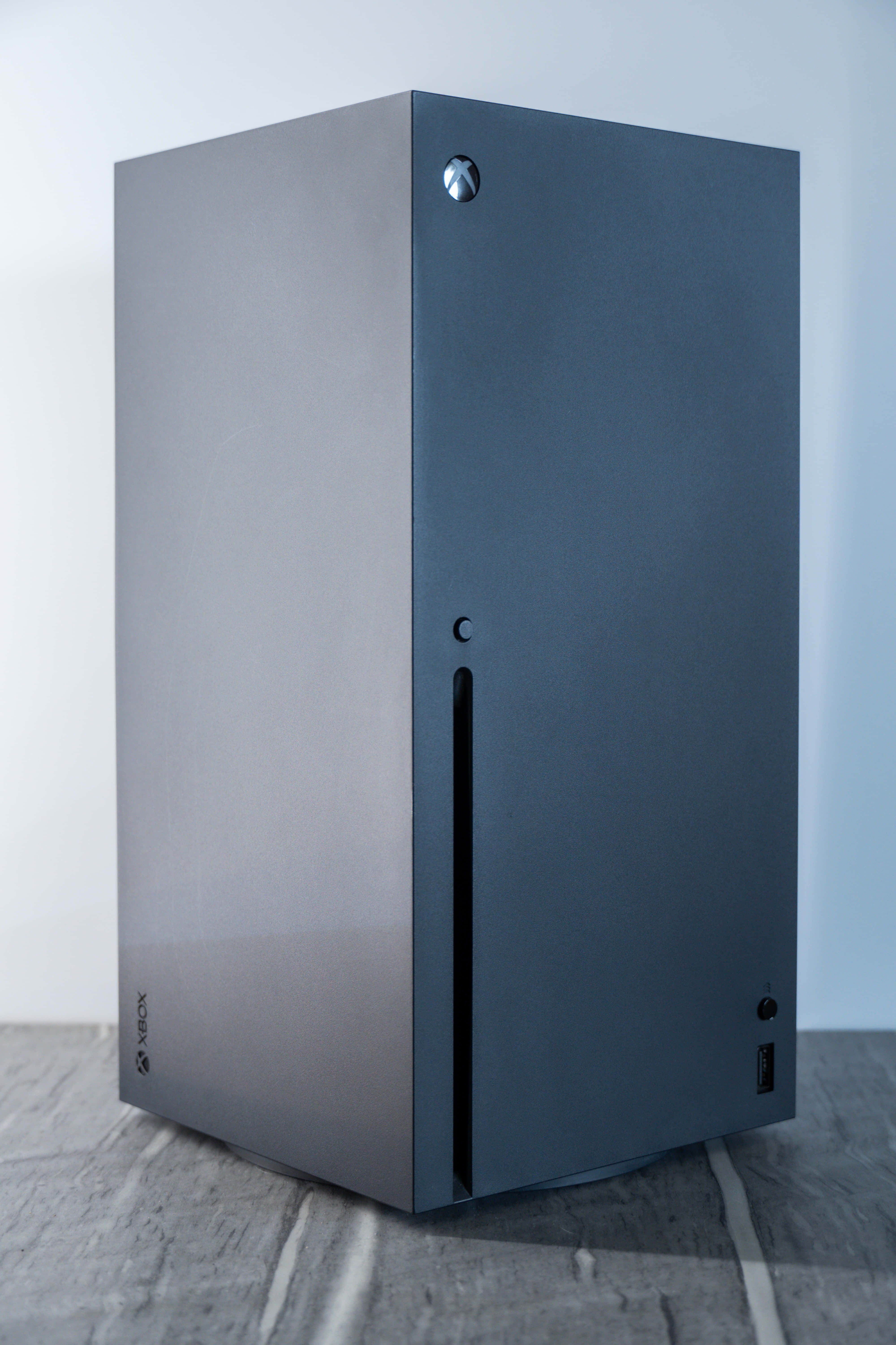 Gaming Consoles 桌布 壁紙 — 一部時尚的磨砂黑色 Xbox Series X 主機直立於灰色瓷磚地板上，背景為純白牆壁。
