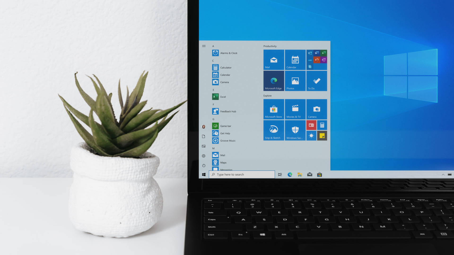 microsoft 桌布 壁紙 — 一部時尚的筆記型電腦在簡約白色桌子上，於盆栽多肉植物旁邊顯示Windows開始功能表。