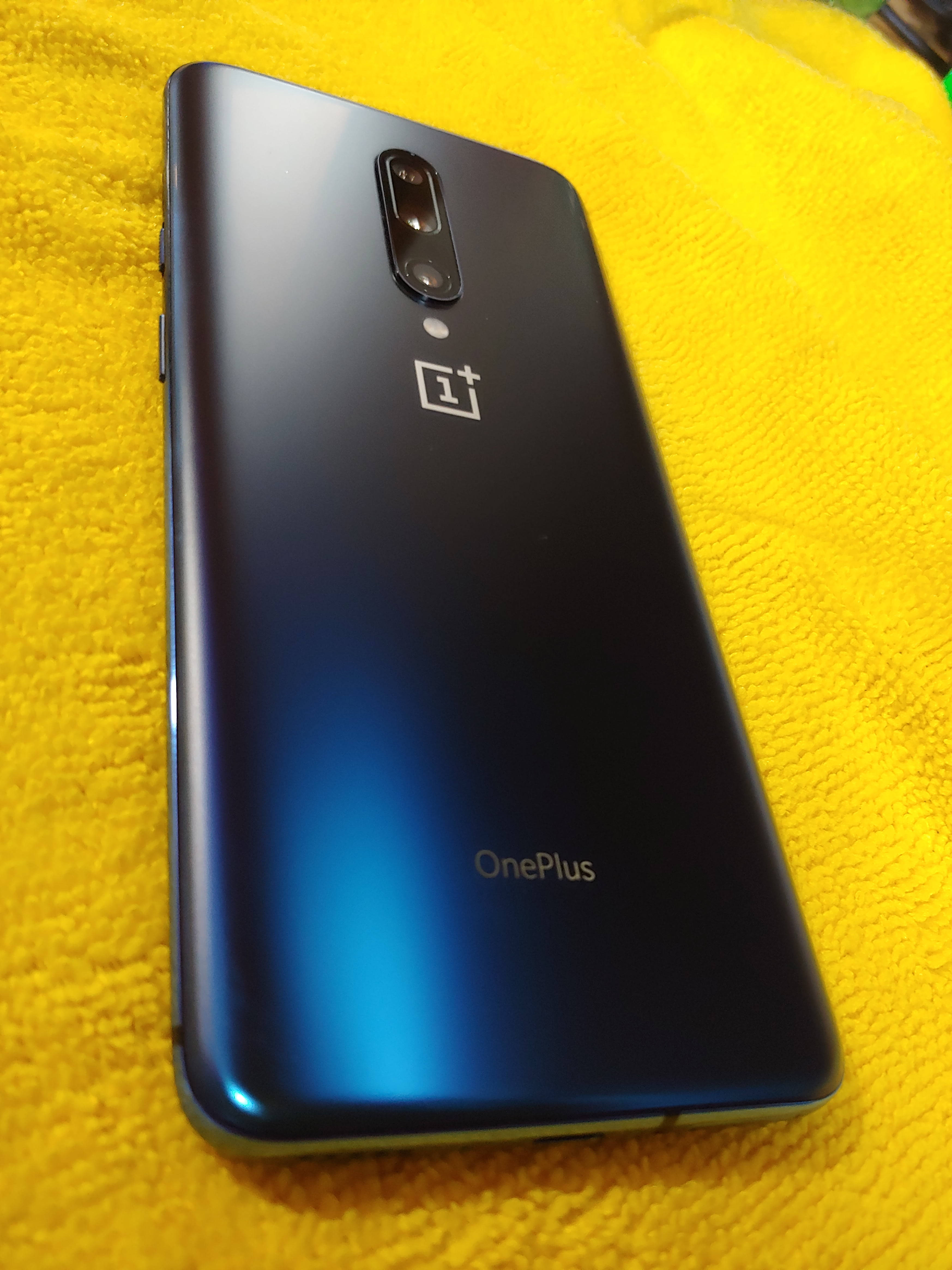 手機 桌布 壁紙 — 一部時尚的藍色 OnePlus 智能手機放在鮮黃色紋理毛巾上，相機和標誌清晰可見。